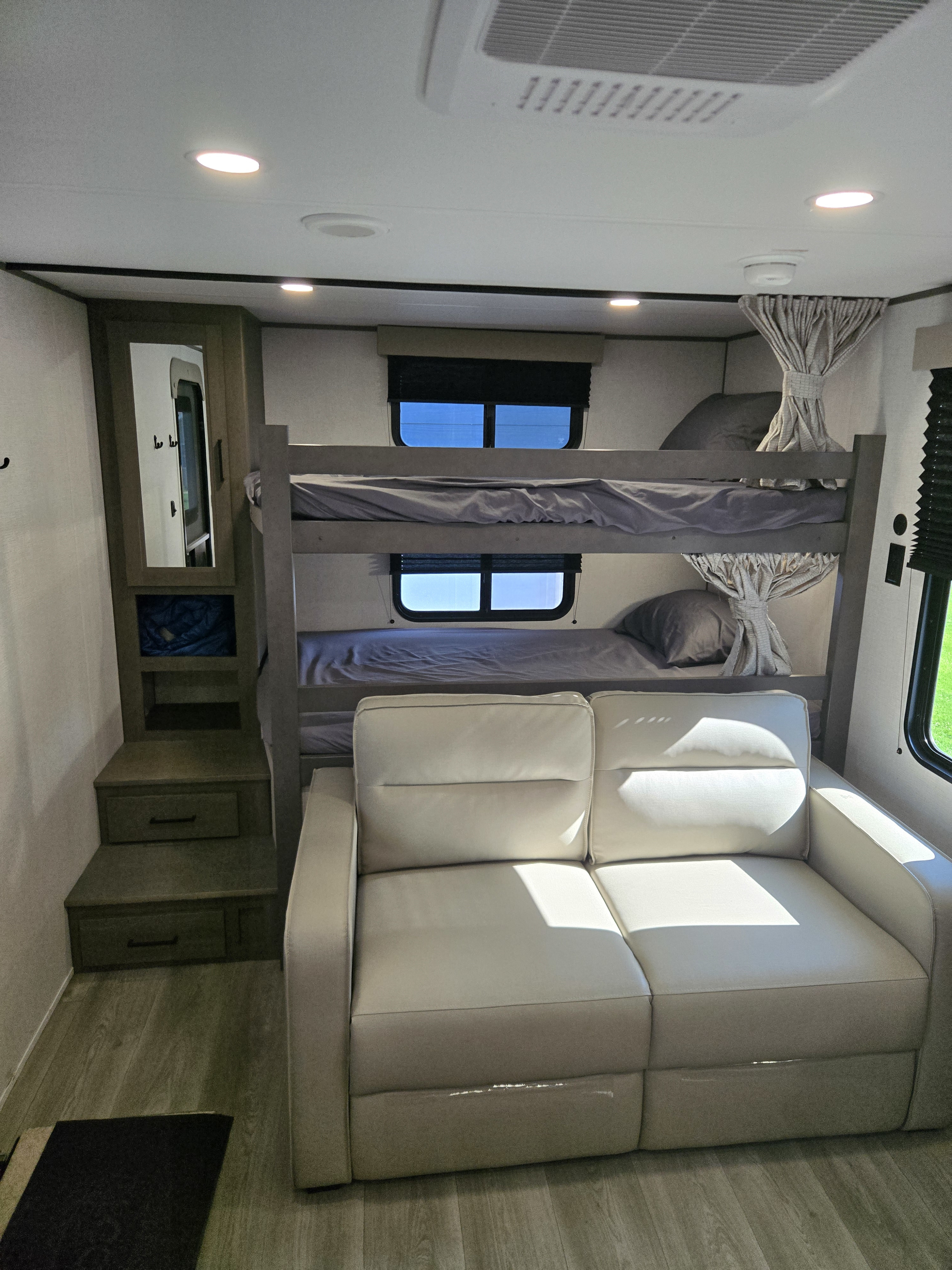 RV rental interior featuring bunk beds, a comfortable light-colored sofa, and built-in storage/stairs.. Grand Design Transcend 2026