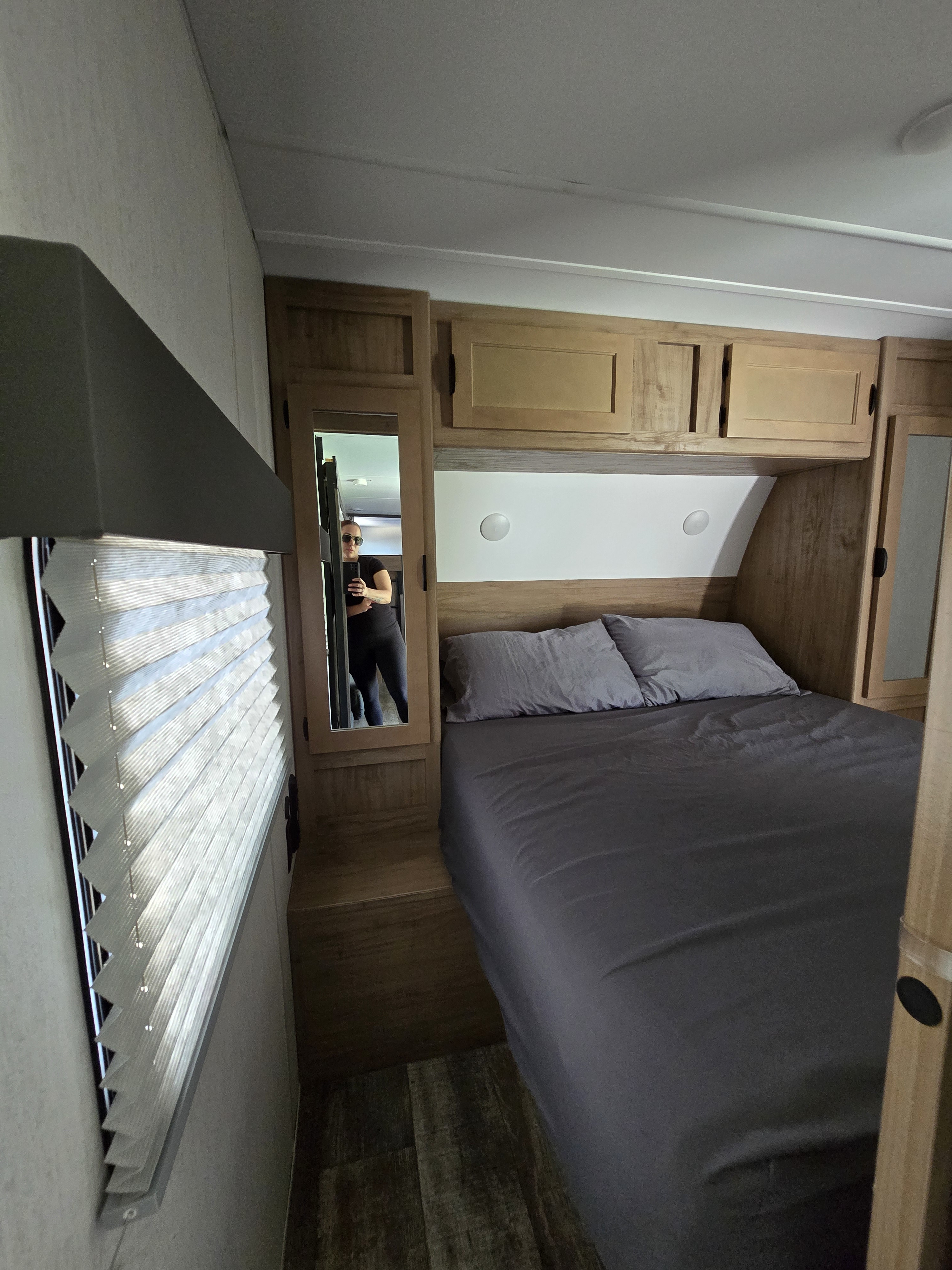 RV rental bedroom interior featuring a comfortable bed with dark gray bedding, wood cabinetry, and a mirror.. Forest River Grey Wolf 2024