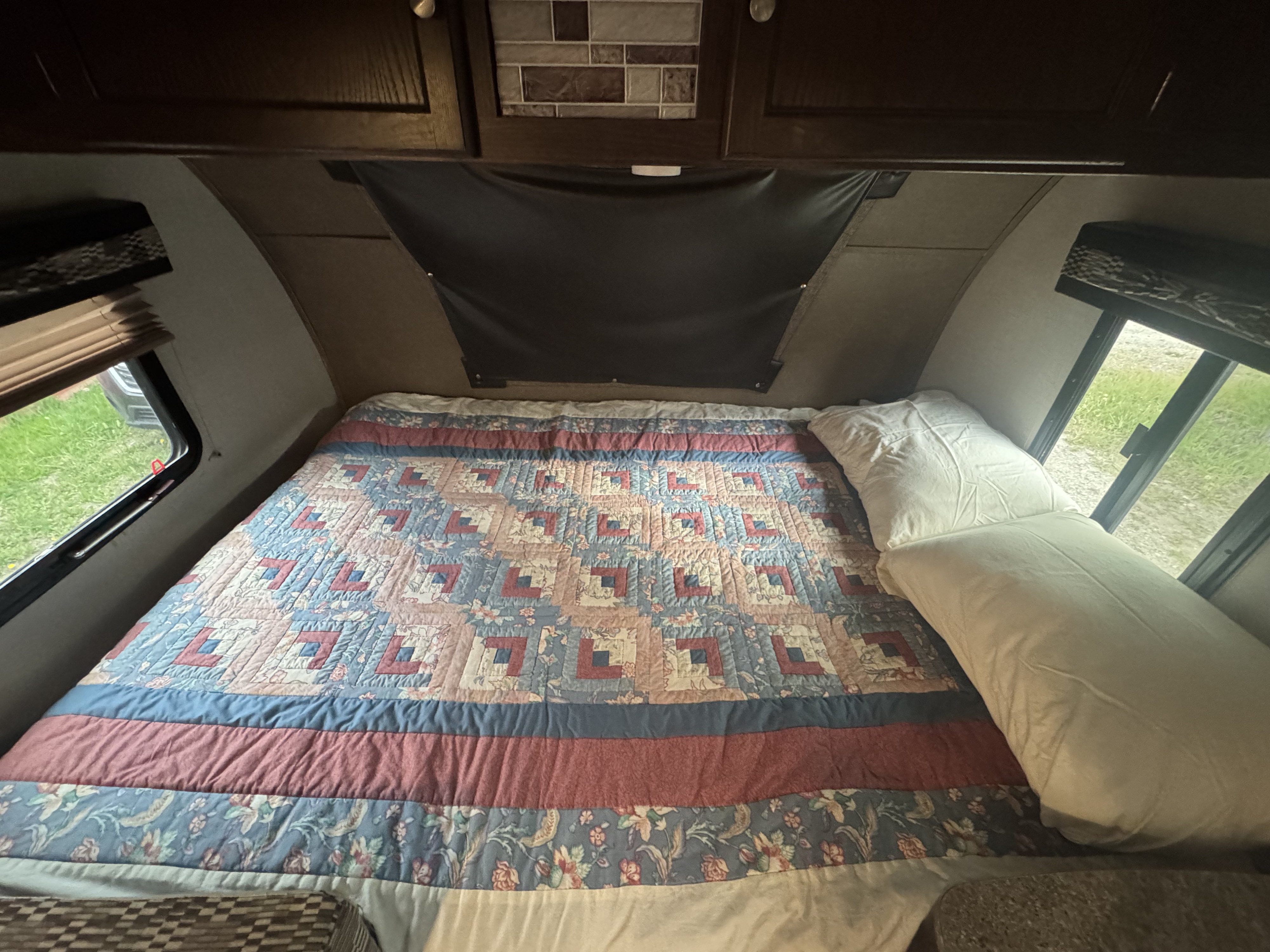 Cozy RV rental bedroom featuring a colorful patterned quilt, white pillows, and side windows with green views.. Forest River Palomino Palomini 2018