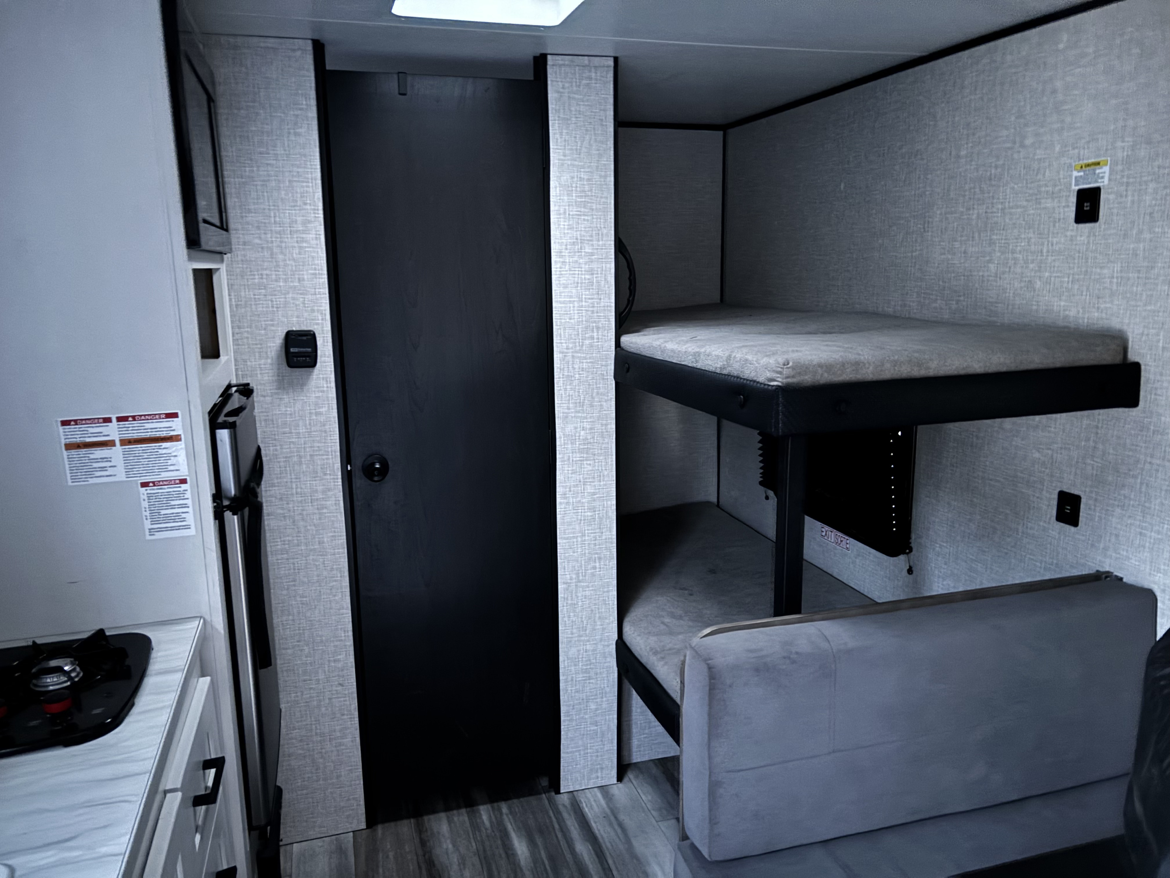 RV rental interior: Compact kitchen with stove/fridge, dark door, and bunk beds with seating below. Perfect for family adventures.. Jayco Jay Flight SLX 2025