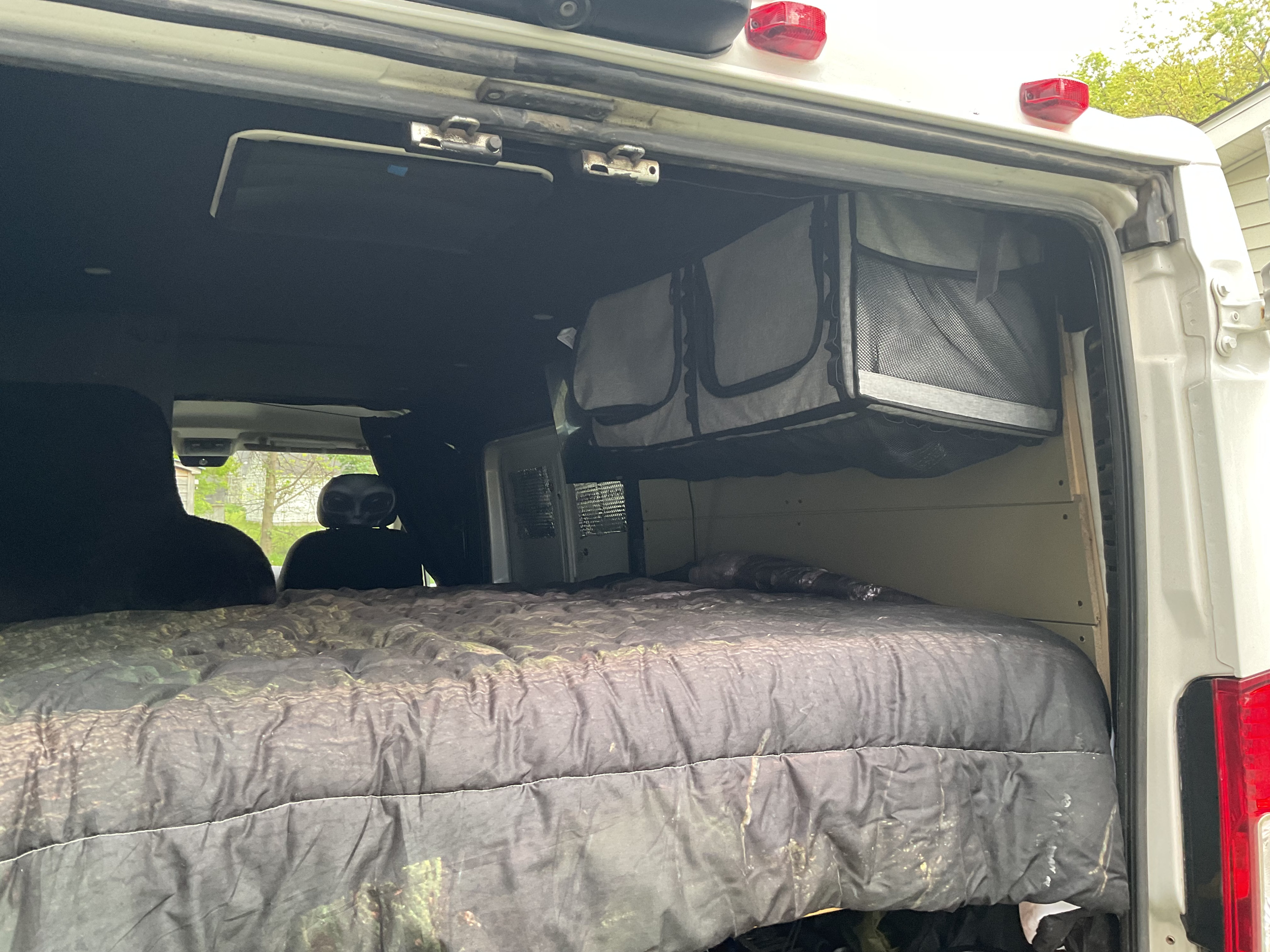 Inside an rv rental camper van: comfortable bed, overhead mesh storage, and unique cabin details visible in the rear.. Ram Promaster 2015
