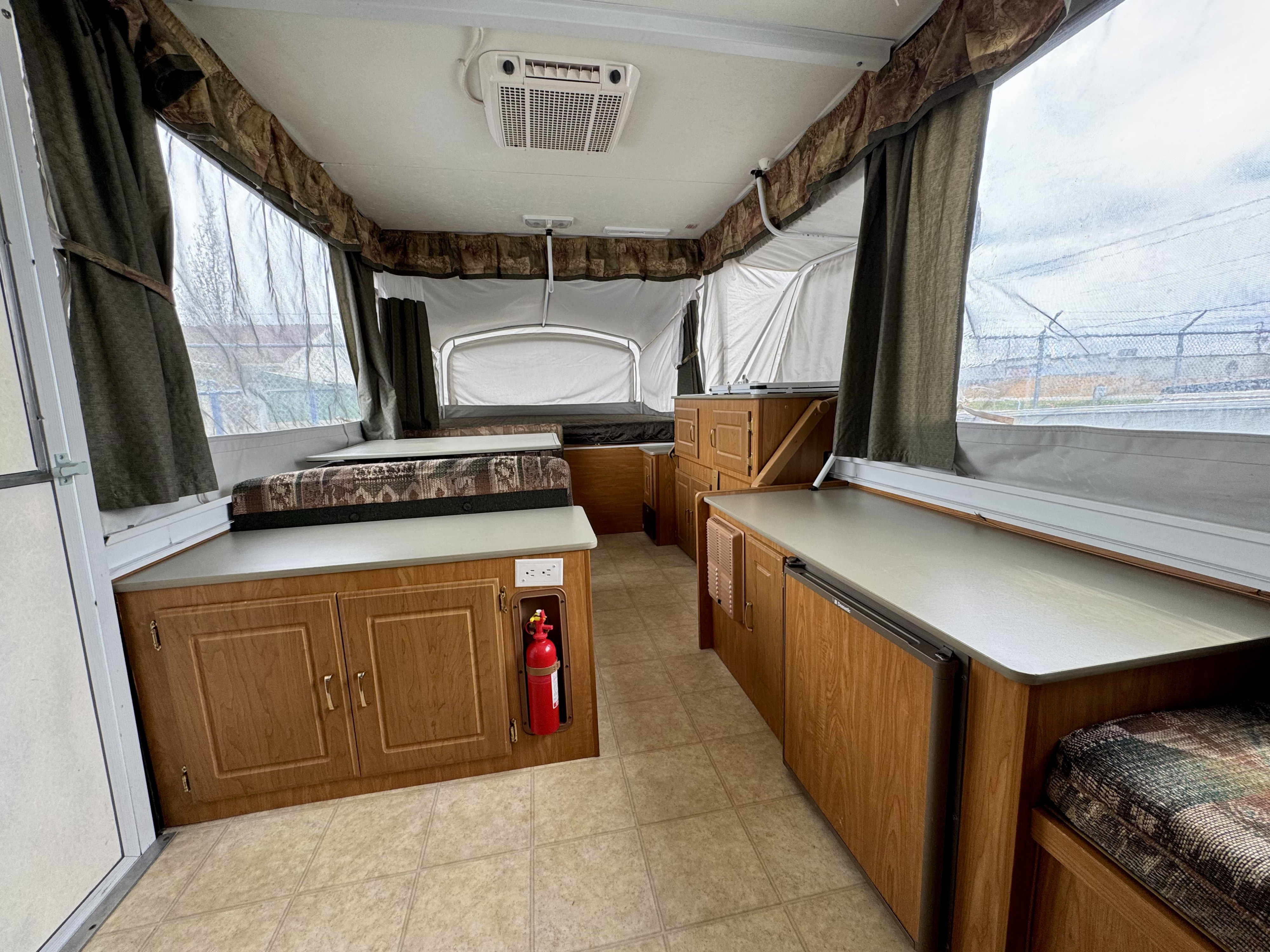 Pop-up RV rental interior: Cozy space with patterned dinette, beds, wood cabinets, counters, fridge, and AC.. Fleetwood RV Mesa 3851 2004