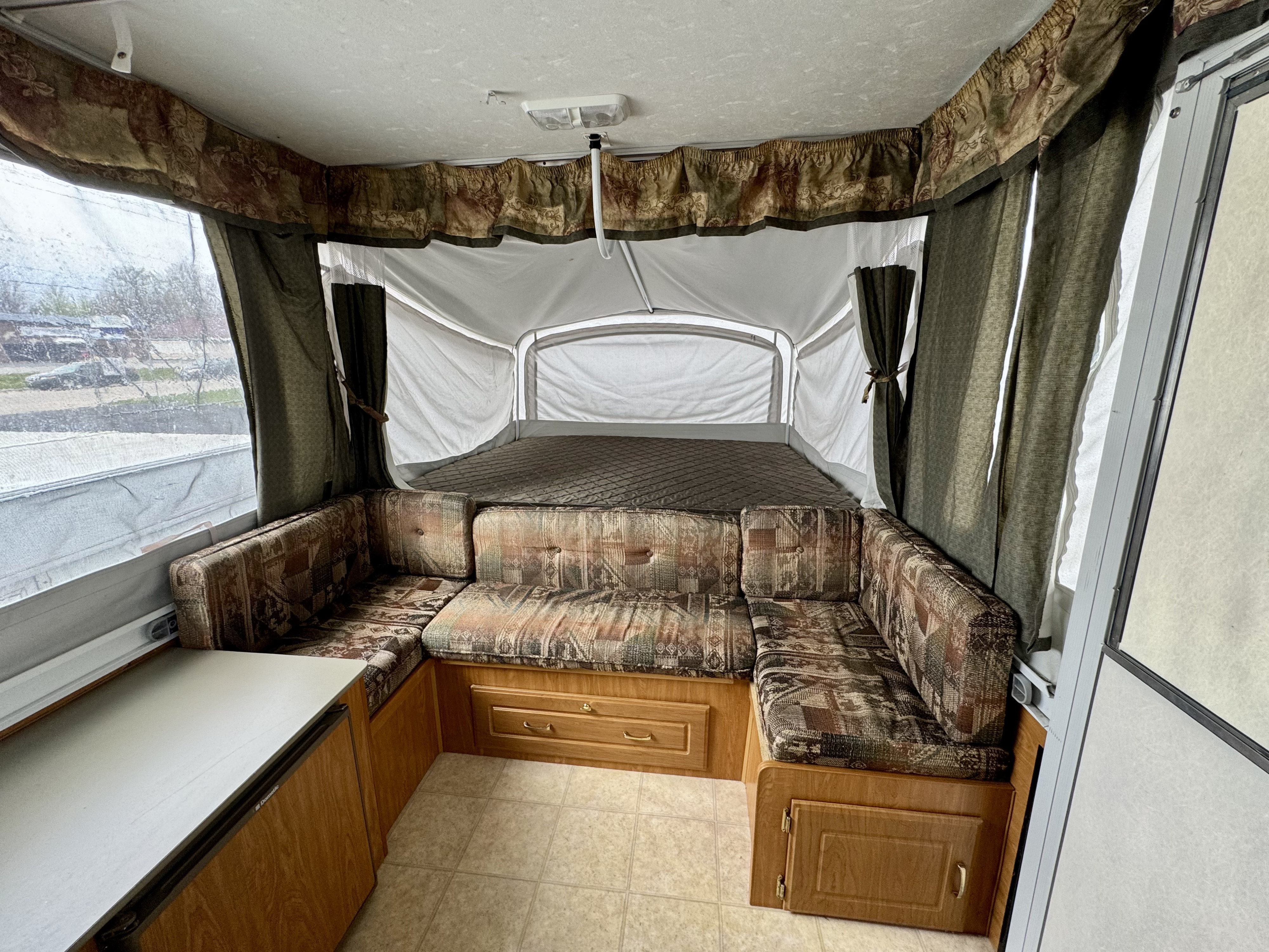 RV rental pop-up camper interior: dinette, bed, and storage. Features patterned cushions and canvas walls.. Fleetwood RV Mesa 3851 2004