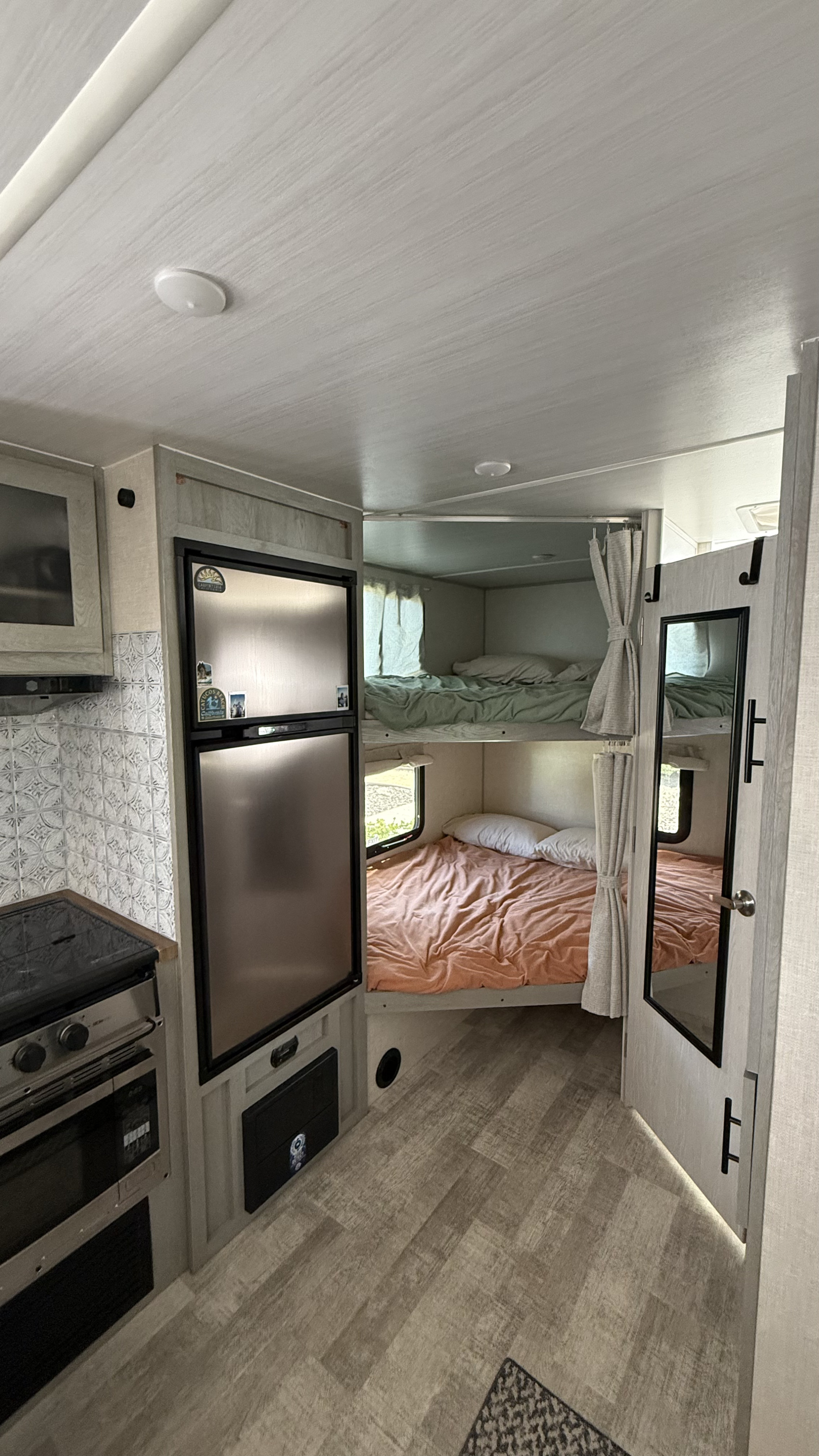 Bright rv rental interior featuring bunk beds, a kitchen with stove/oven, a stainless steel refrigerator, and wood-look flooring.. Forest River Ibex Essentials+ Only 2023