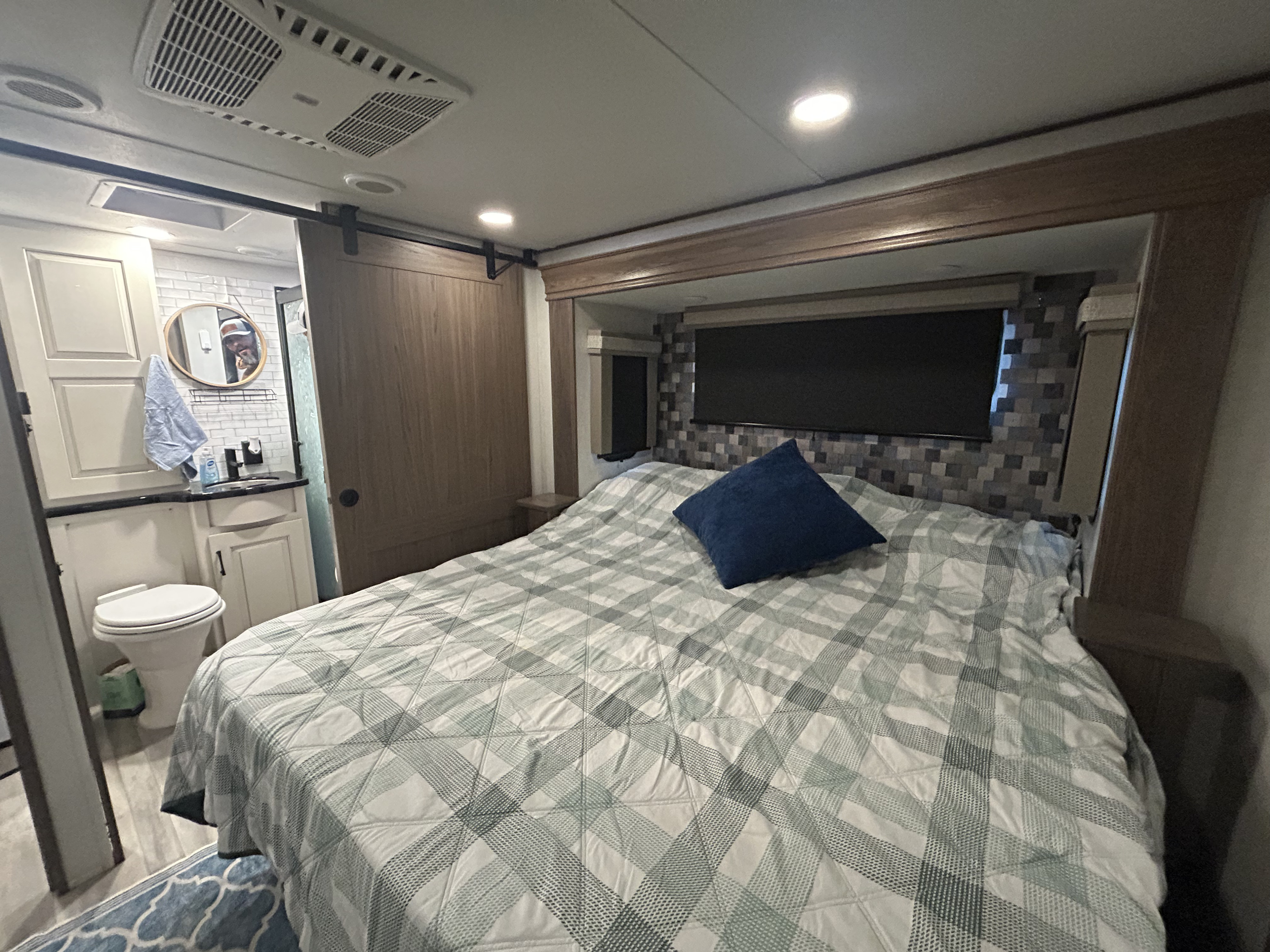 Spacious RV rental bedroom featuring a queen bed with plaid quilt, modern ensuite bathroom, and barn door.. Alliance RV Paradigm 2023
