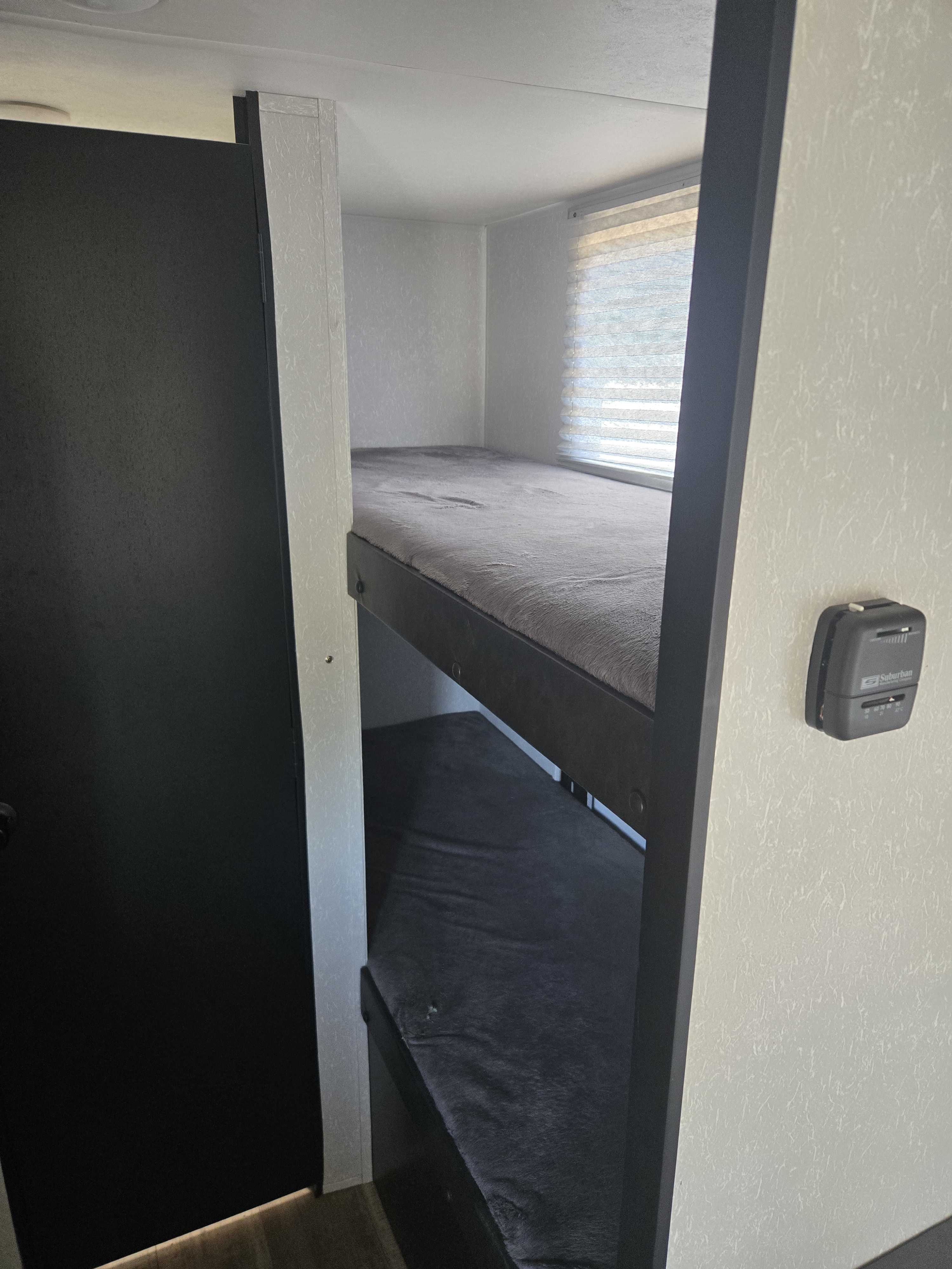 RV rental interior with comfortable bunk beds, featuring soft grey mattresses, a window, and a thermostat.. Forest River Cherokee Wolf Pup 2022