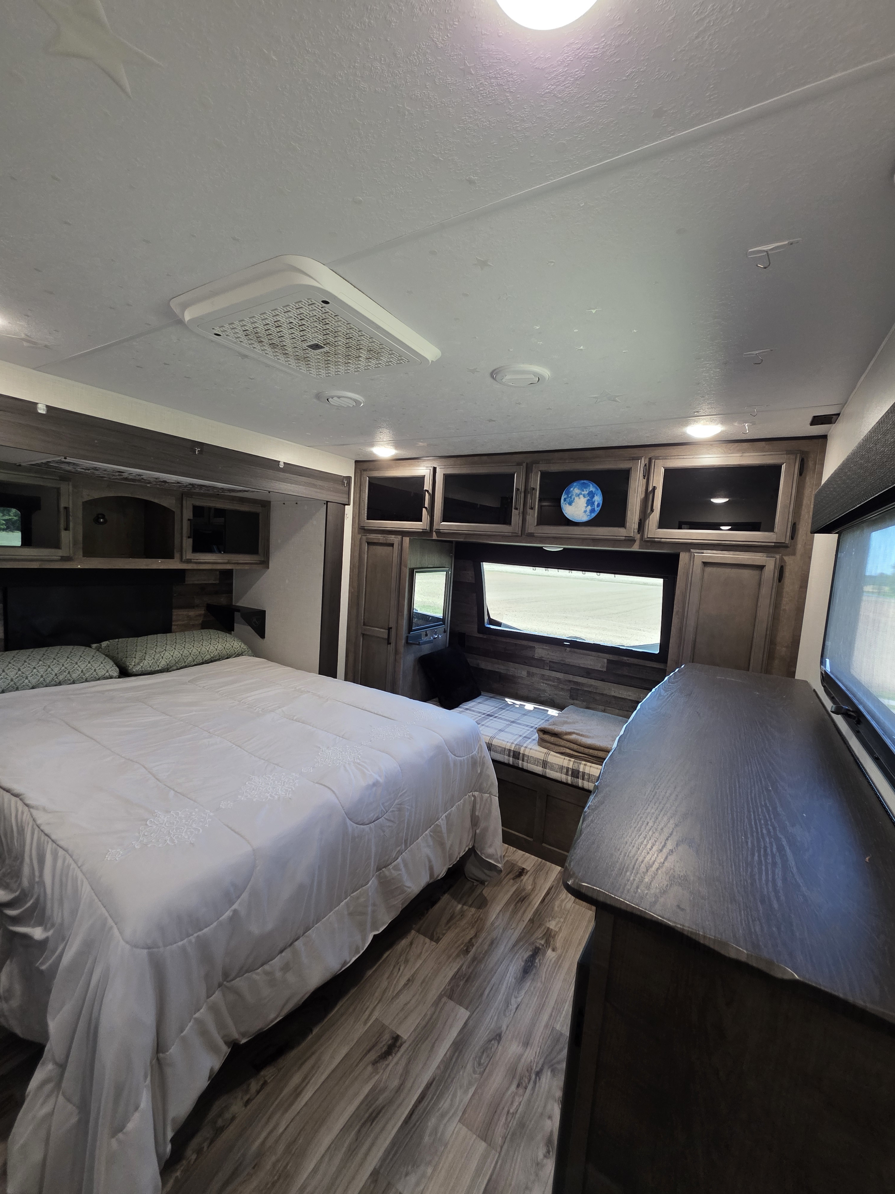 Inside a modern rv rental bedroom: queen bed, wood cabinets, window bench, and dresser. Textured ceiling with AC. Perfect for travel comfort.. Sporttrek Touring Edition 2024