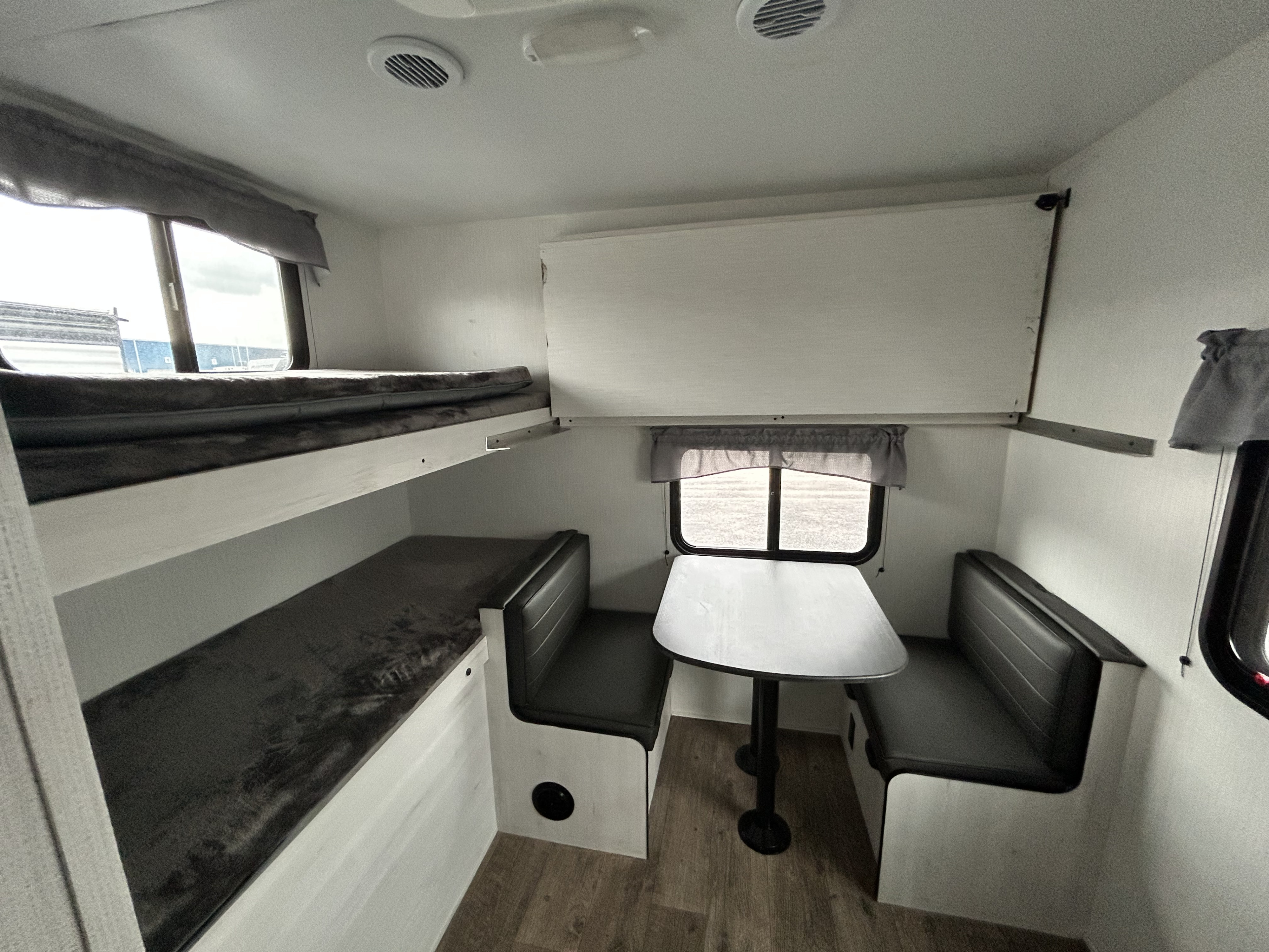 View inside an RV rental: two bunk beds on the left, and a dinette with benches and a table on the right.. Heartland RVs Trail Runner 2024