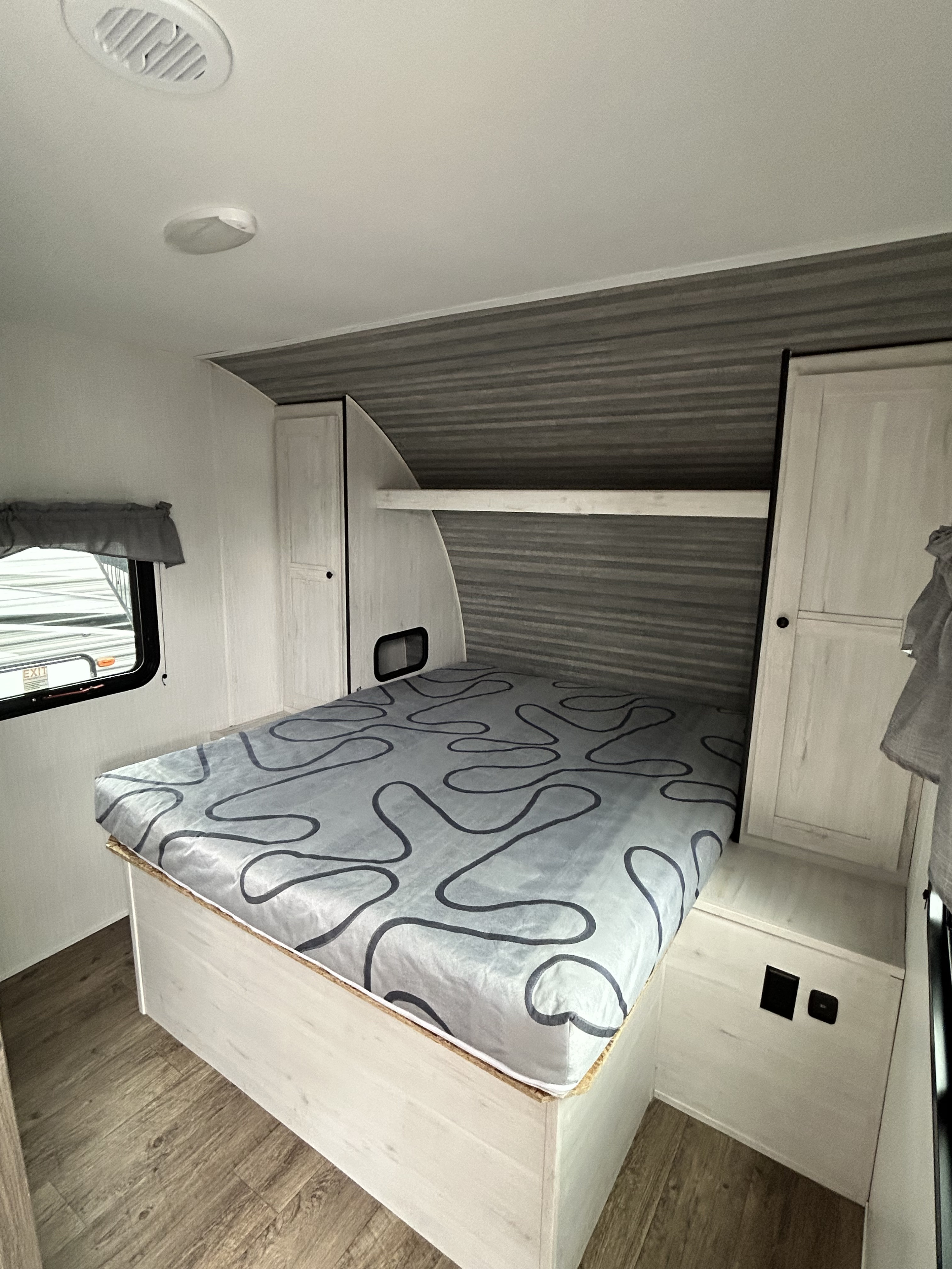 RV rental interior: cozy bedroom with patterned bed, built-in cabinets, and window. Compact sleeping area.. Heartland RVs Trail Runner 2024
