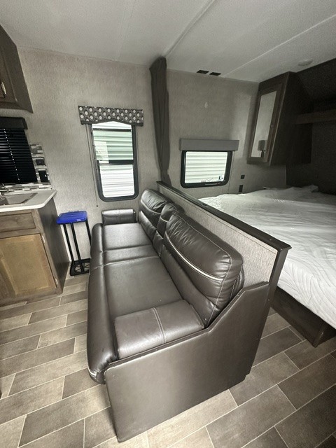 RV rental interior: cozy living area with a brown sofa, bed, and small kitchenette area, featuring patterned flooring.. Dutchmen Coleman Lantern LT 2020