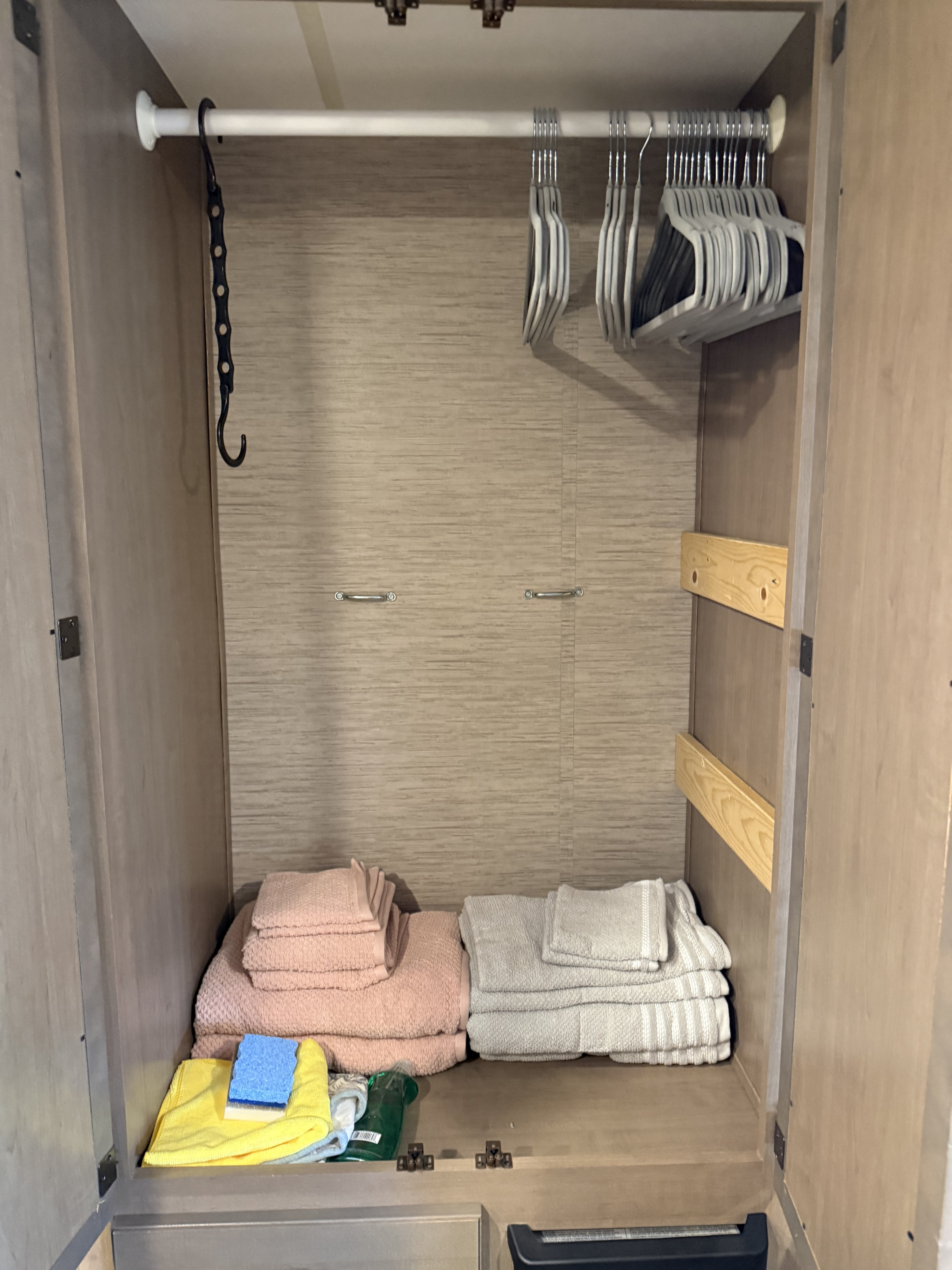Inside an RV rental closet: a hanging rod with hangers, neatly folded towels, and cleaning supplies on the bottom shelf.. Thor Chateau 2022