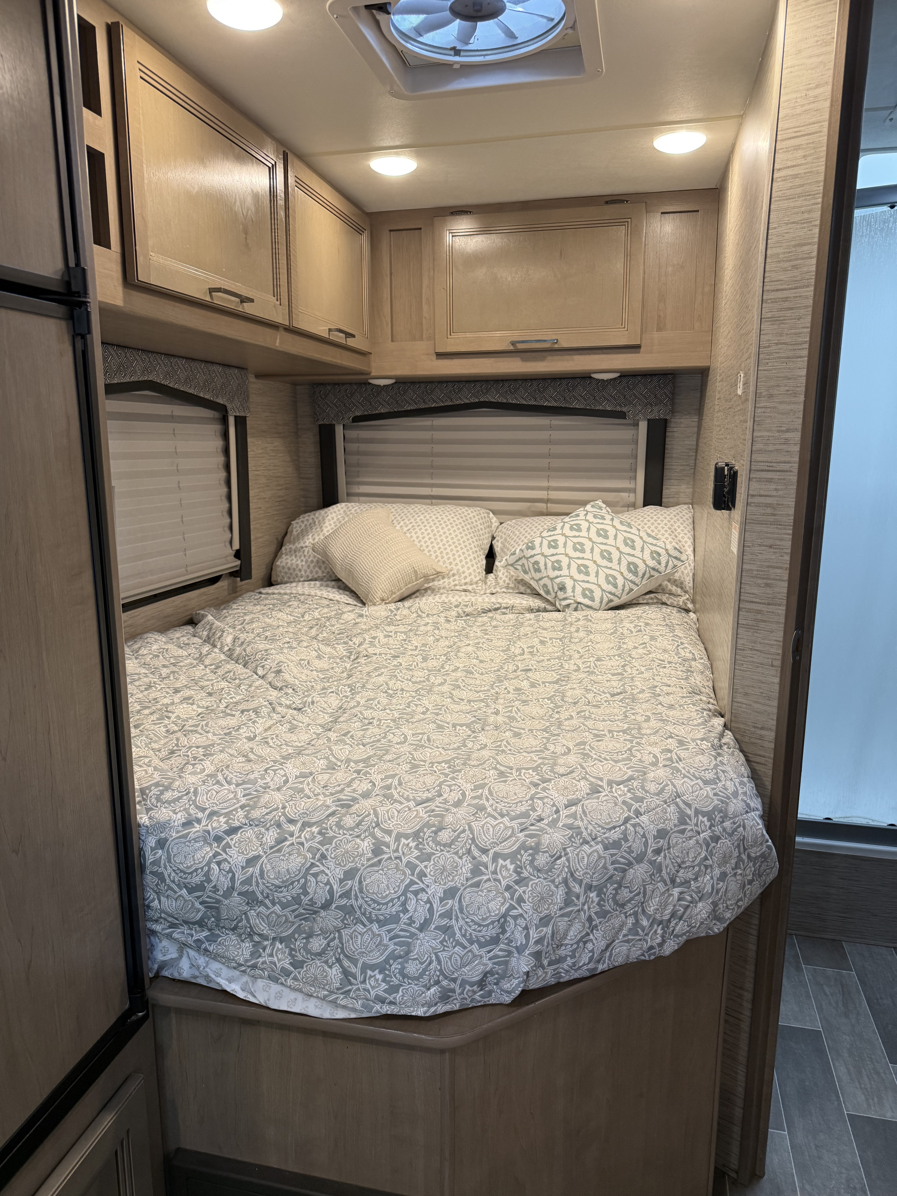 RV rental bedroom with a patterned bed, pillows, overhead cabinets, window blinds, and a ceiling vent.. Thor Chateau 2022