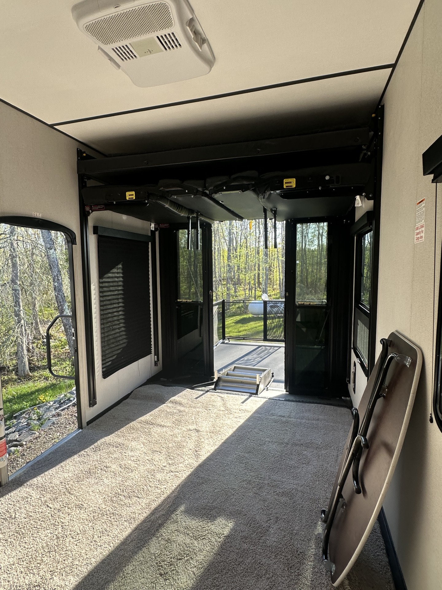 RV rental toy hauler interior with open rear ramp to outdoor deck, carpeted floor, and folded overhead bunk.. Keystone RV Fuzion Toy Hauler 2022