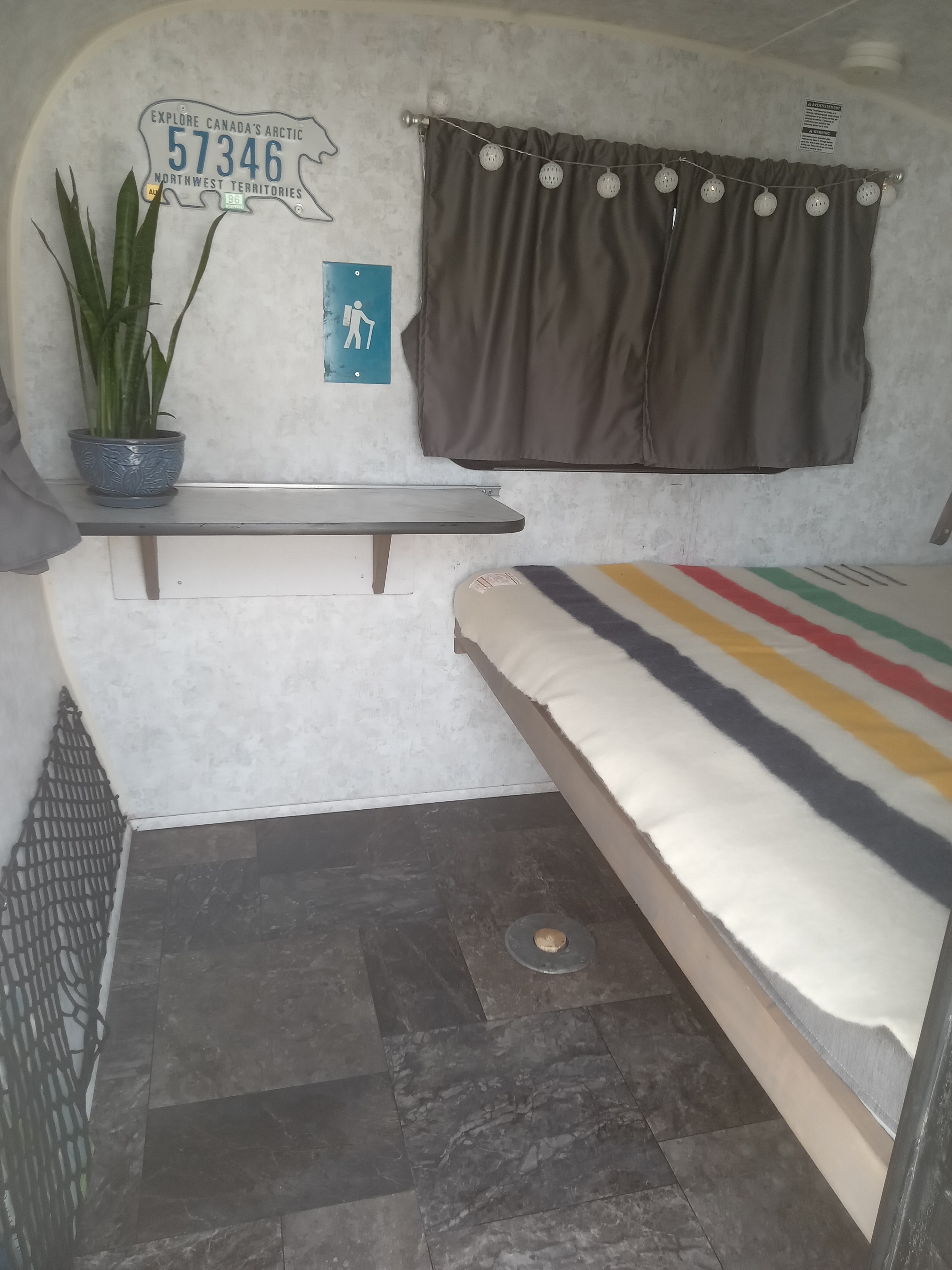 Inside a charming rv rental: bed with colorful blanket, potted plant, and a polar bear-shaped Northwest Territories license plate.. Prolite Prolite Trailer 2018