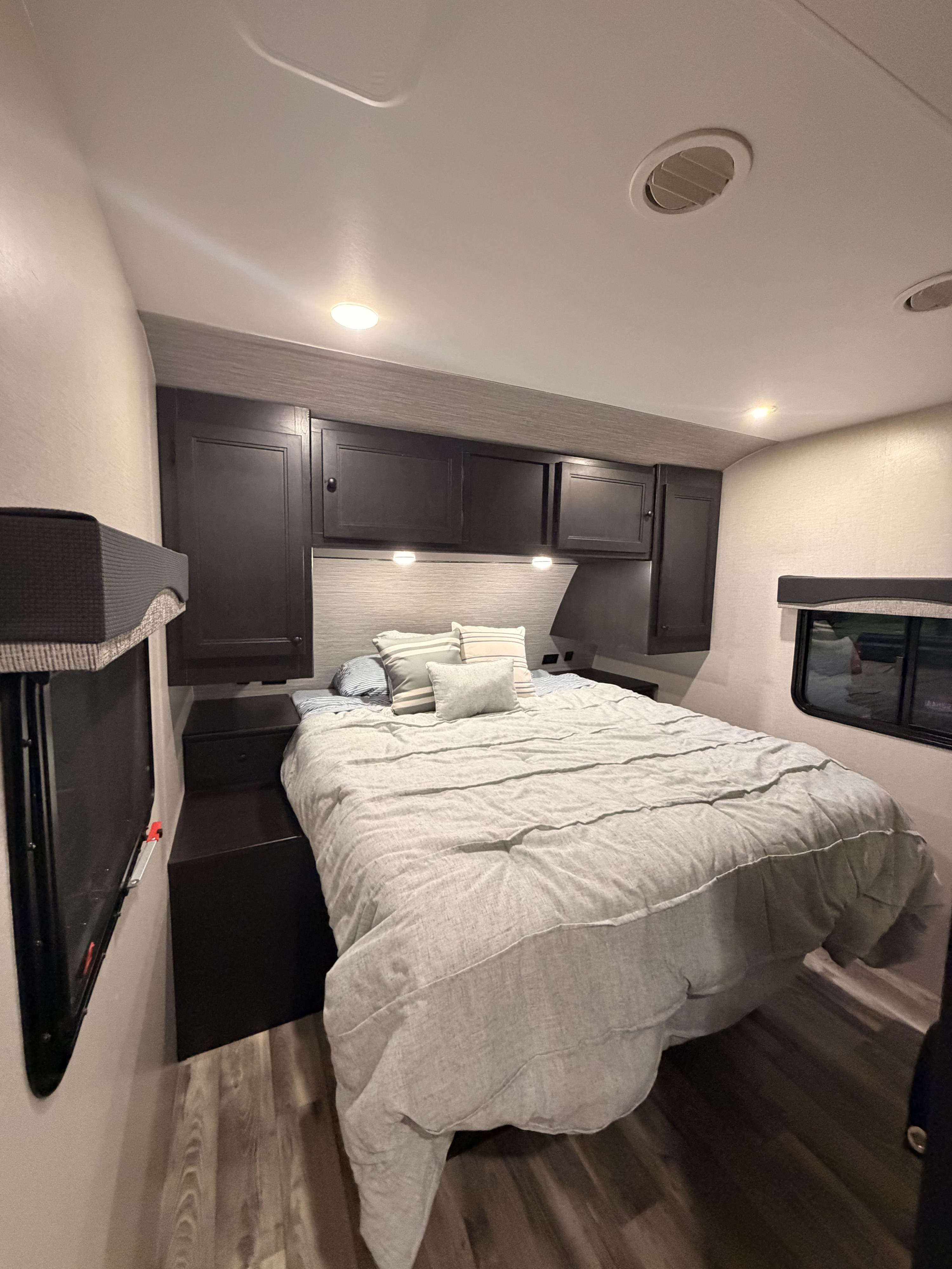 RV rental: A cozy, modern bedroom featuring a bed with light gray bedding, dark cabinets, small windows, and wood-look floors.. Starcraft Super Lite 2022