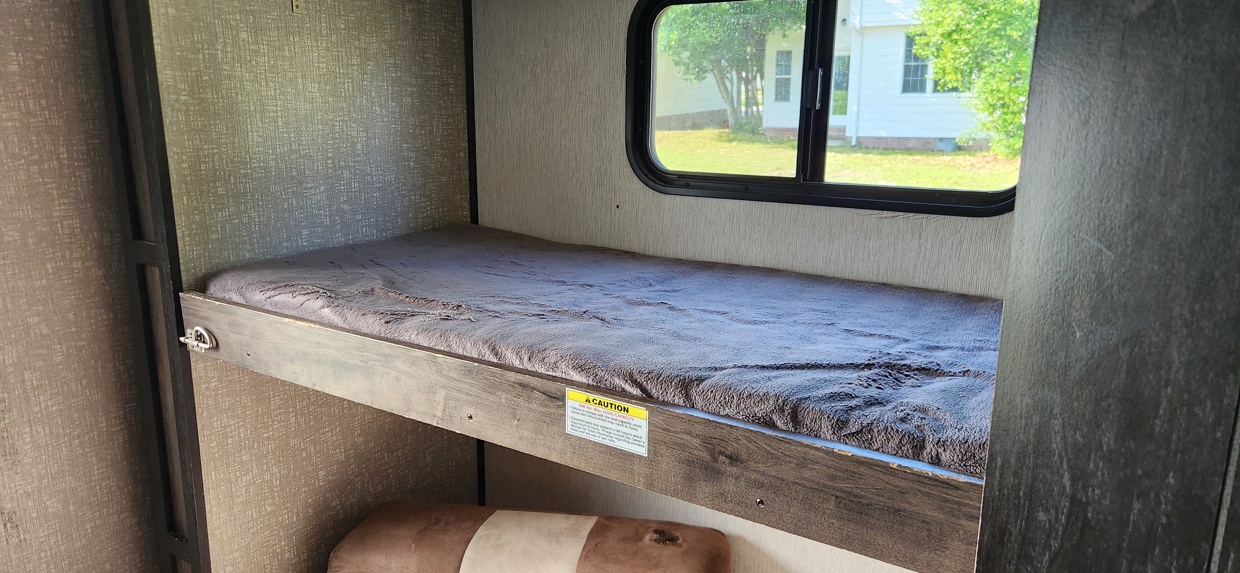Comfortable RV rental bunk bed interior with fluffy bedding, a bright window view, and a visible safety warning.. Heartland RVs Mallard 2019