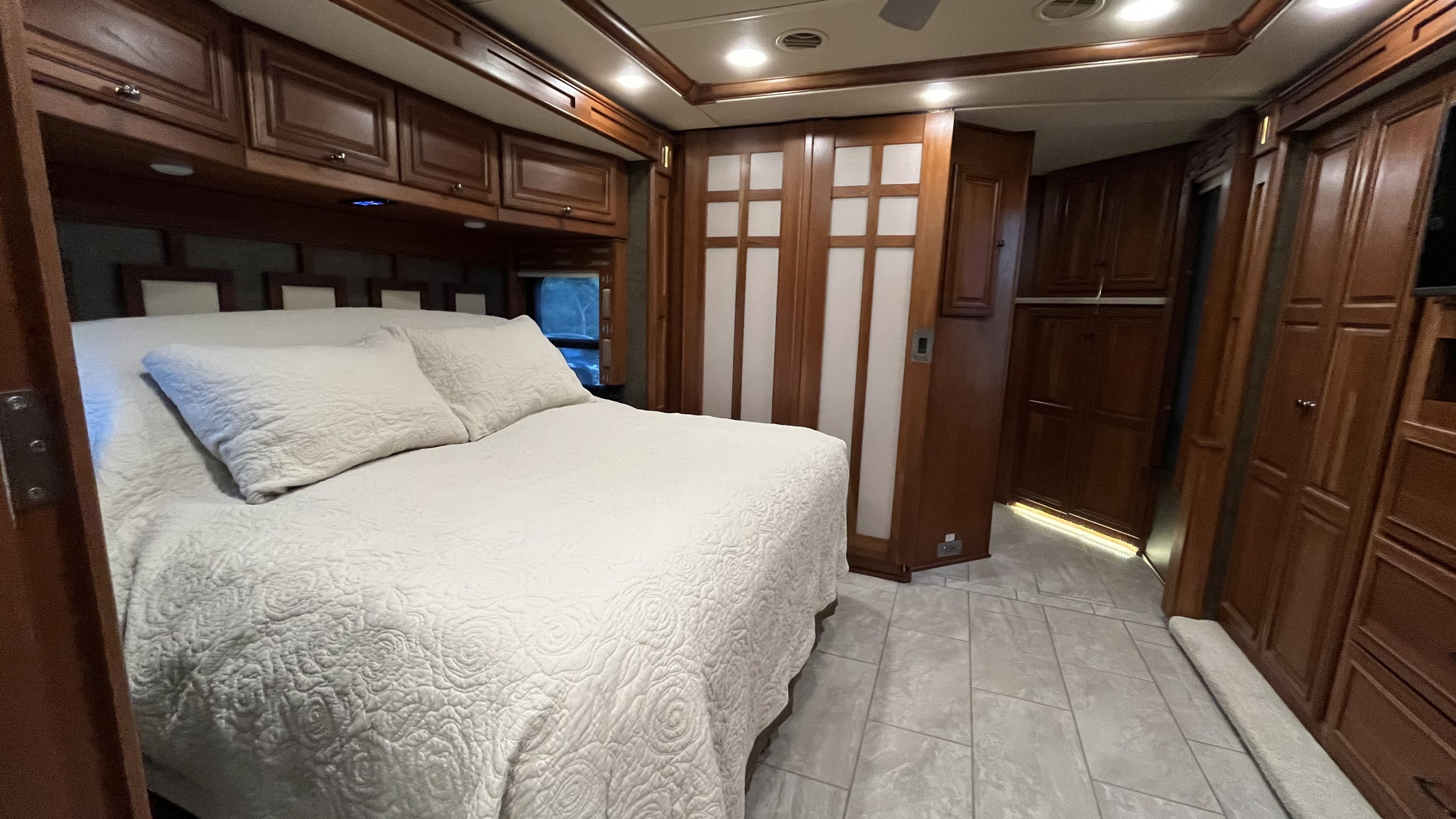 Spacious RV rental bedroom with a large bed, dark wood cabinets, and modern tile flooring. Ideal for comfortable travel.. Winnebago Tour 2016