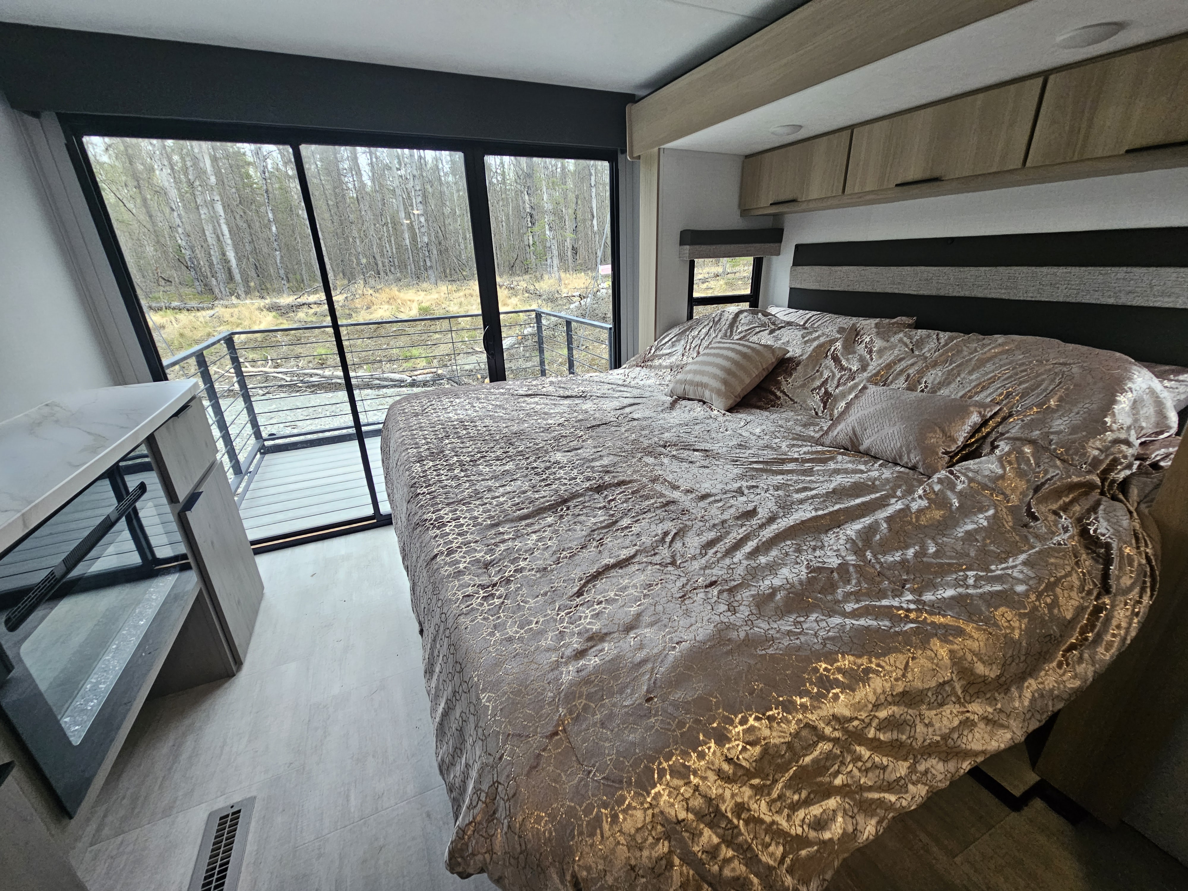 Cozy RV rental bedroom with a large bed, modern interior, and a private deck overlooking a peaceful forest view.. Dutchmen Kodiak Ultimate 2025