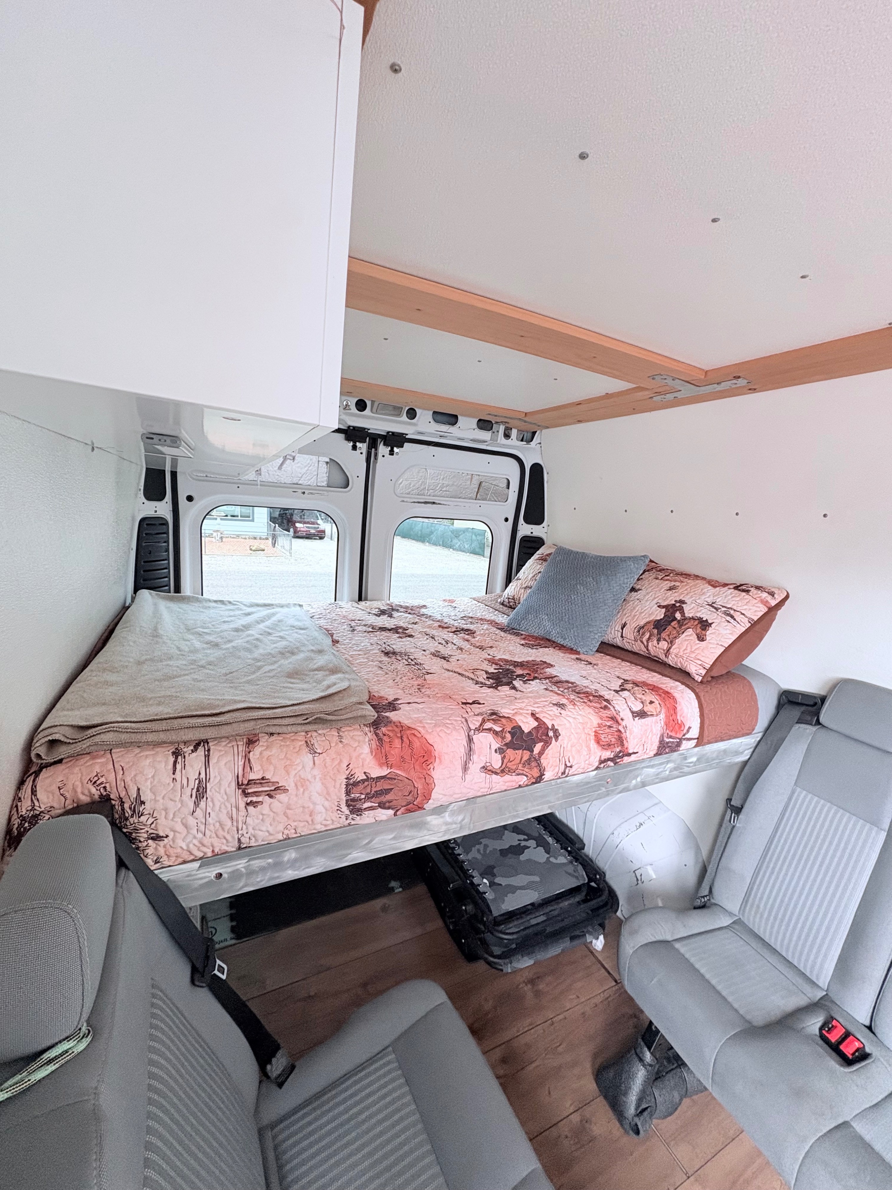 Cozy rv rental camper van interior: elevated bed with western quilt, passenger seating, and under-bed storage.. Dodge 2500 Cargo Van High Roof 159" WB 2019