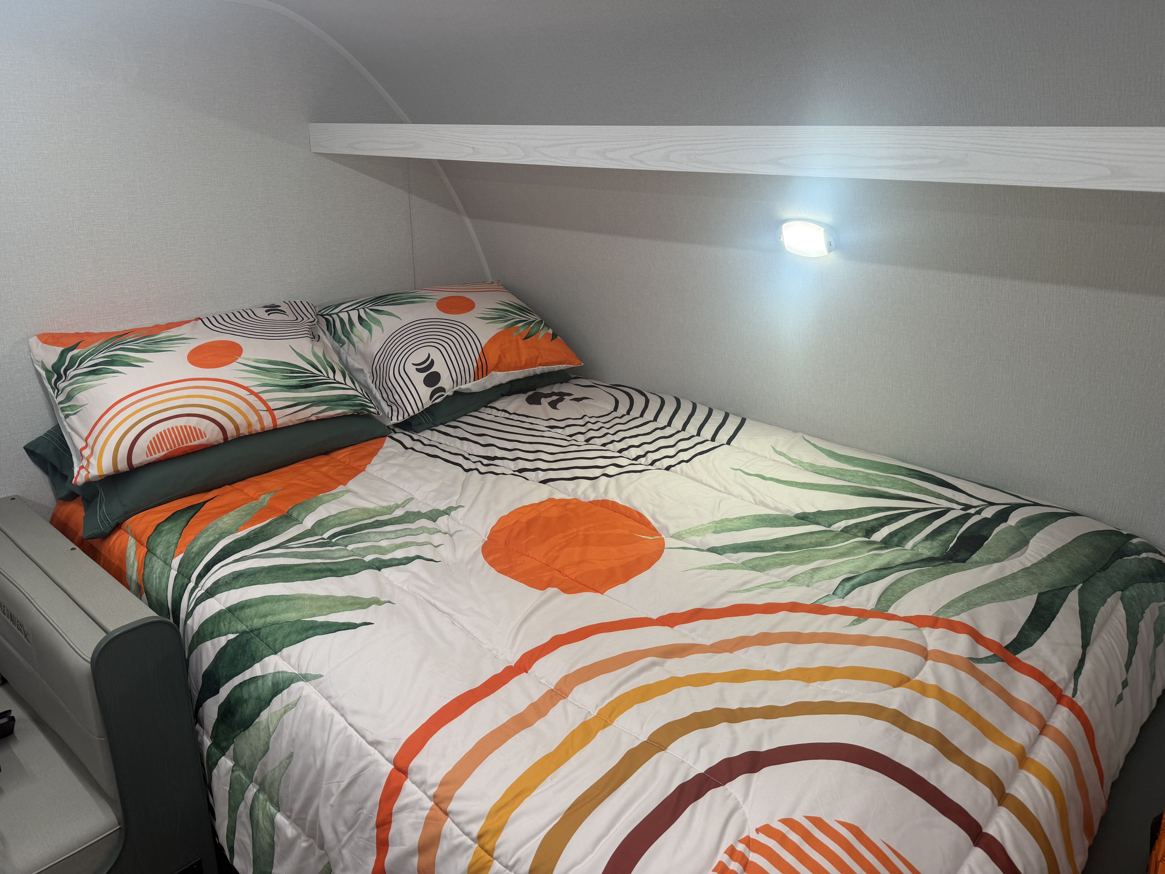 Cozy rv rental bed with vibrant bedding featuring leaves, rainbows, and circles, plus a shelf and wall light.. Heartland RVs Eddie Bauer 2025