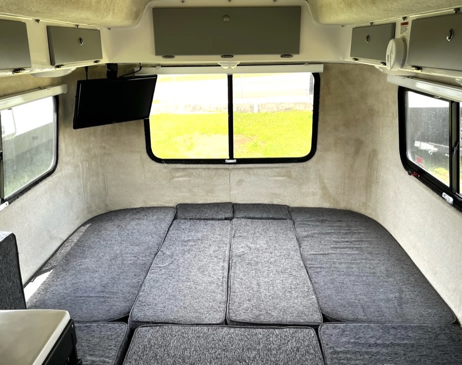 Inside a cozy RV rental: a large gray bed, ample windows, and a TV, ready for your road trip comfort.. Casita Casita Trailer 2022