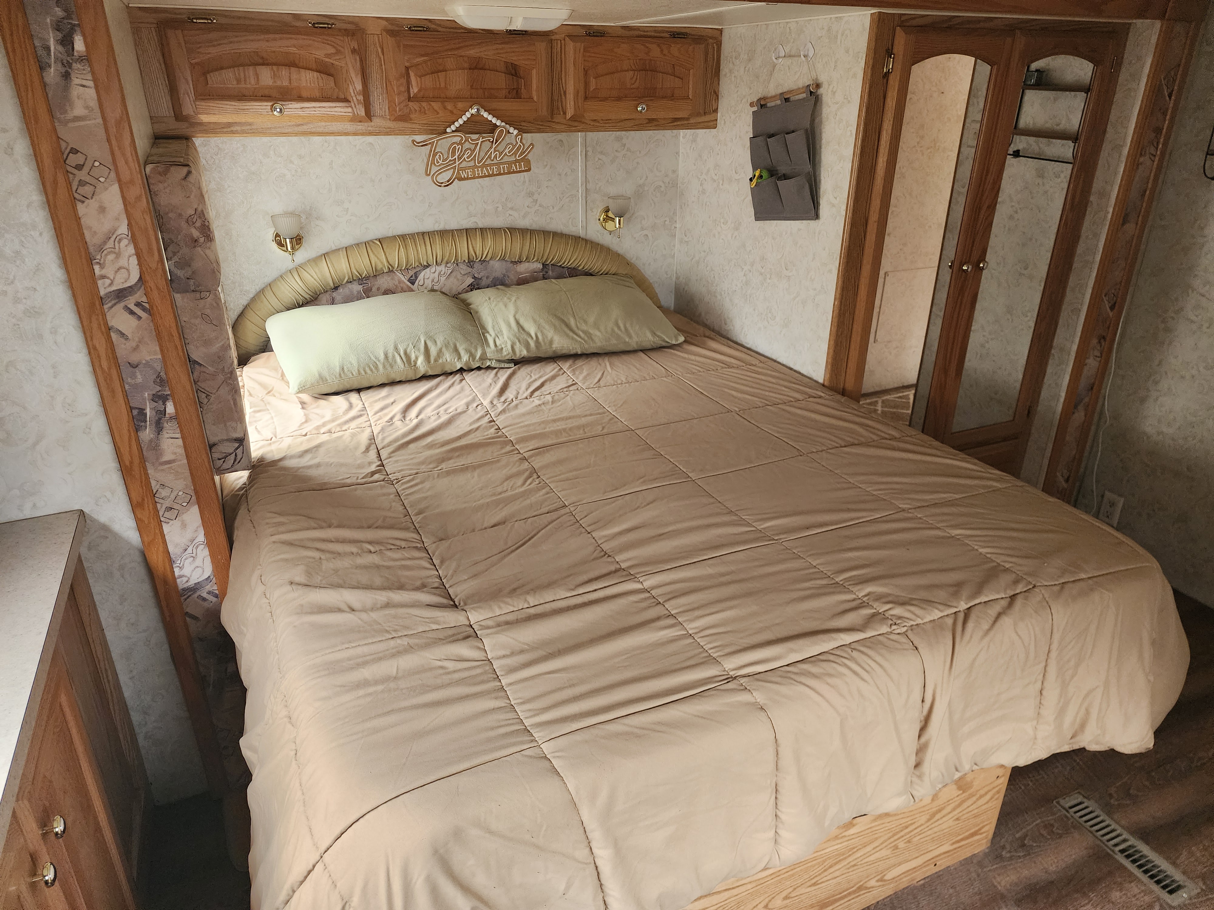 Cozy RV rental bedroom featuring a comfortable bed, overhead cabinets, and decorative wall accents.. Carriage Cameo SEL 2003