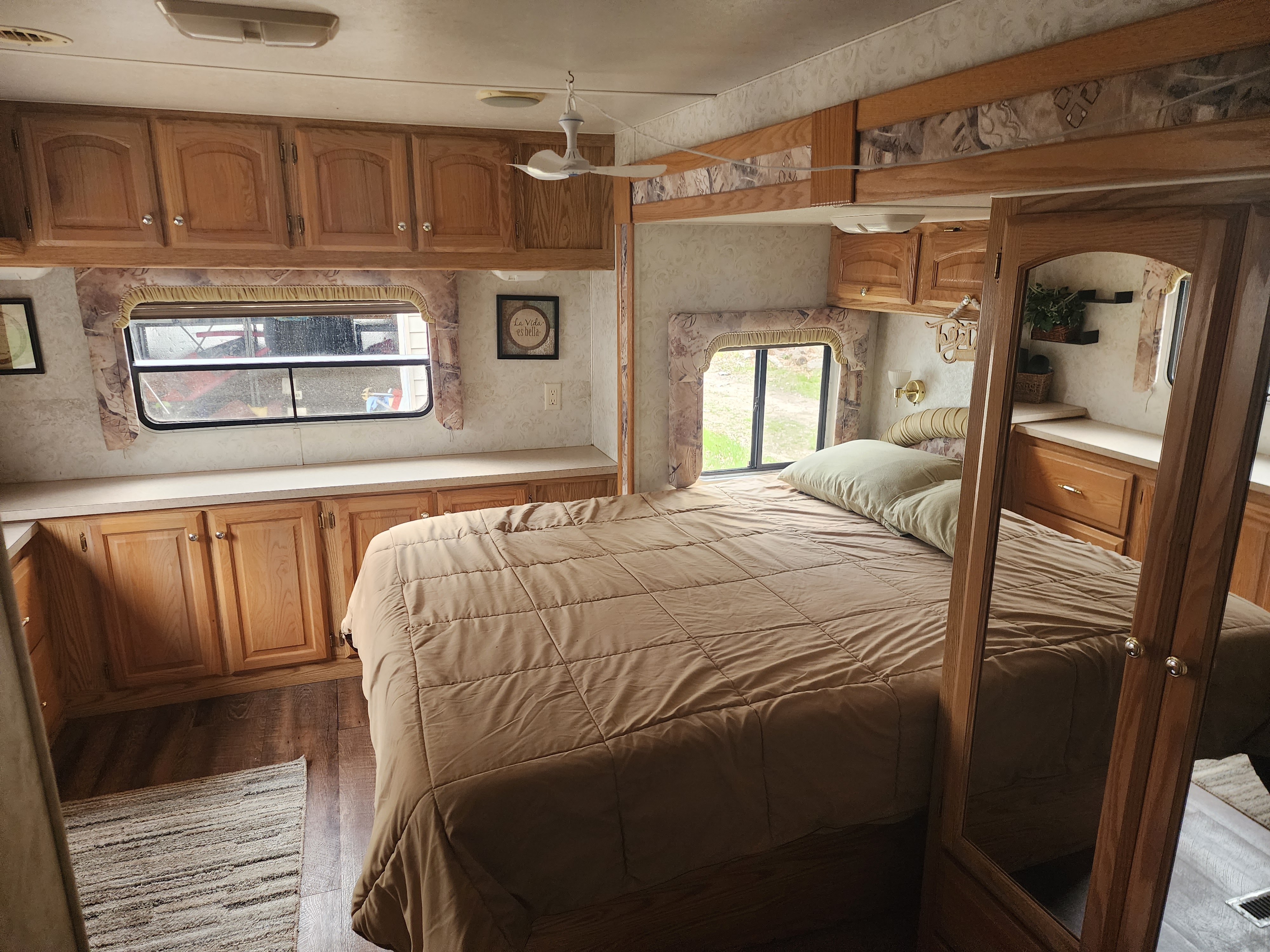 RV rental bedroom with a cozy bed, brown comforter, wood cabinets, windows, and a small ceiling fan.. Carriage Cameo SEL 2003