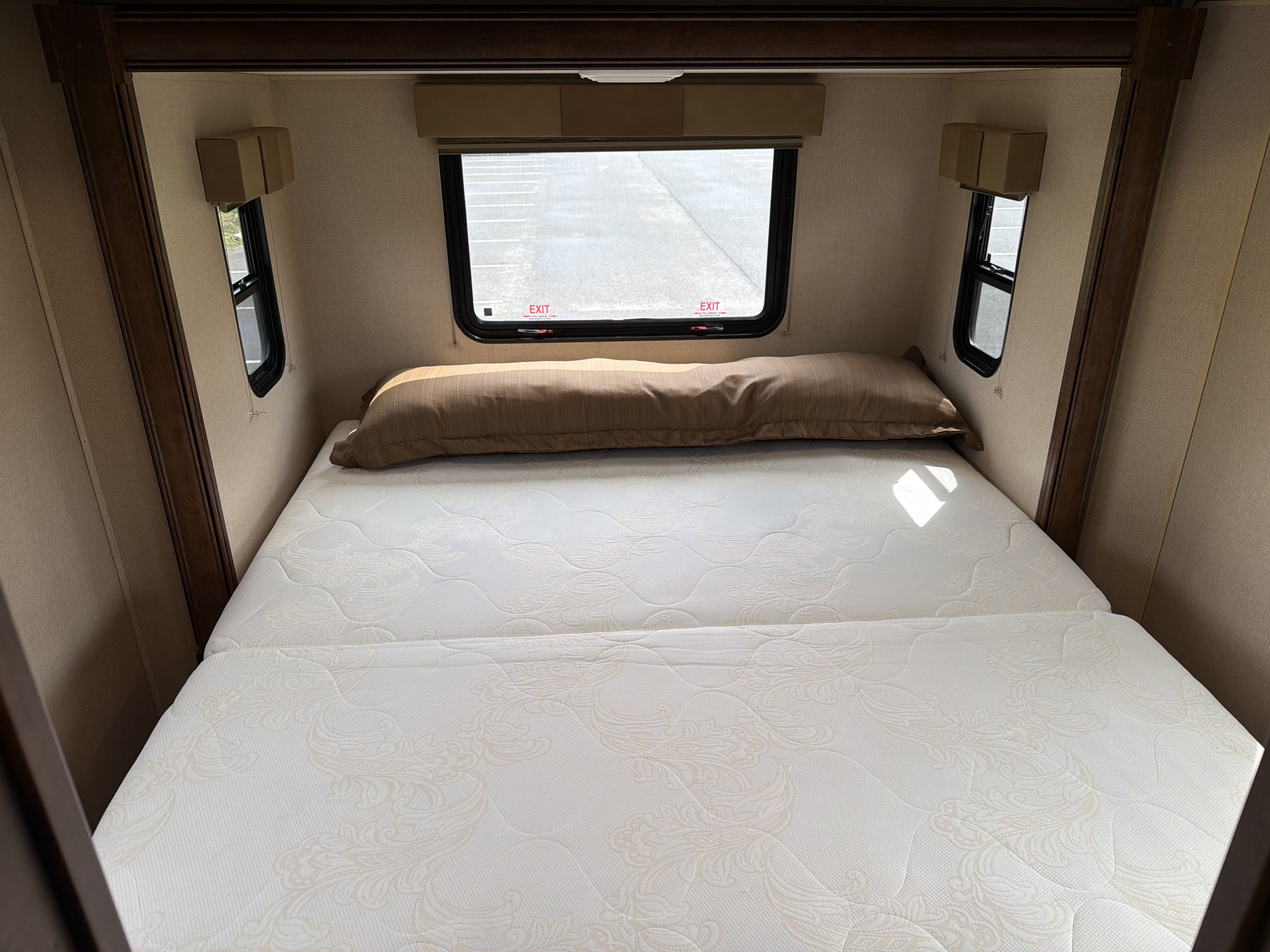 Inside an RV rental, a cozy bedroom features a white patterned mattress, brown pillow, and multiple windows including an emergency exit.. Forest River FR3 2016