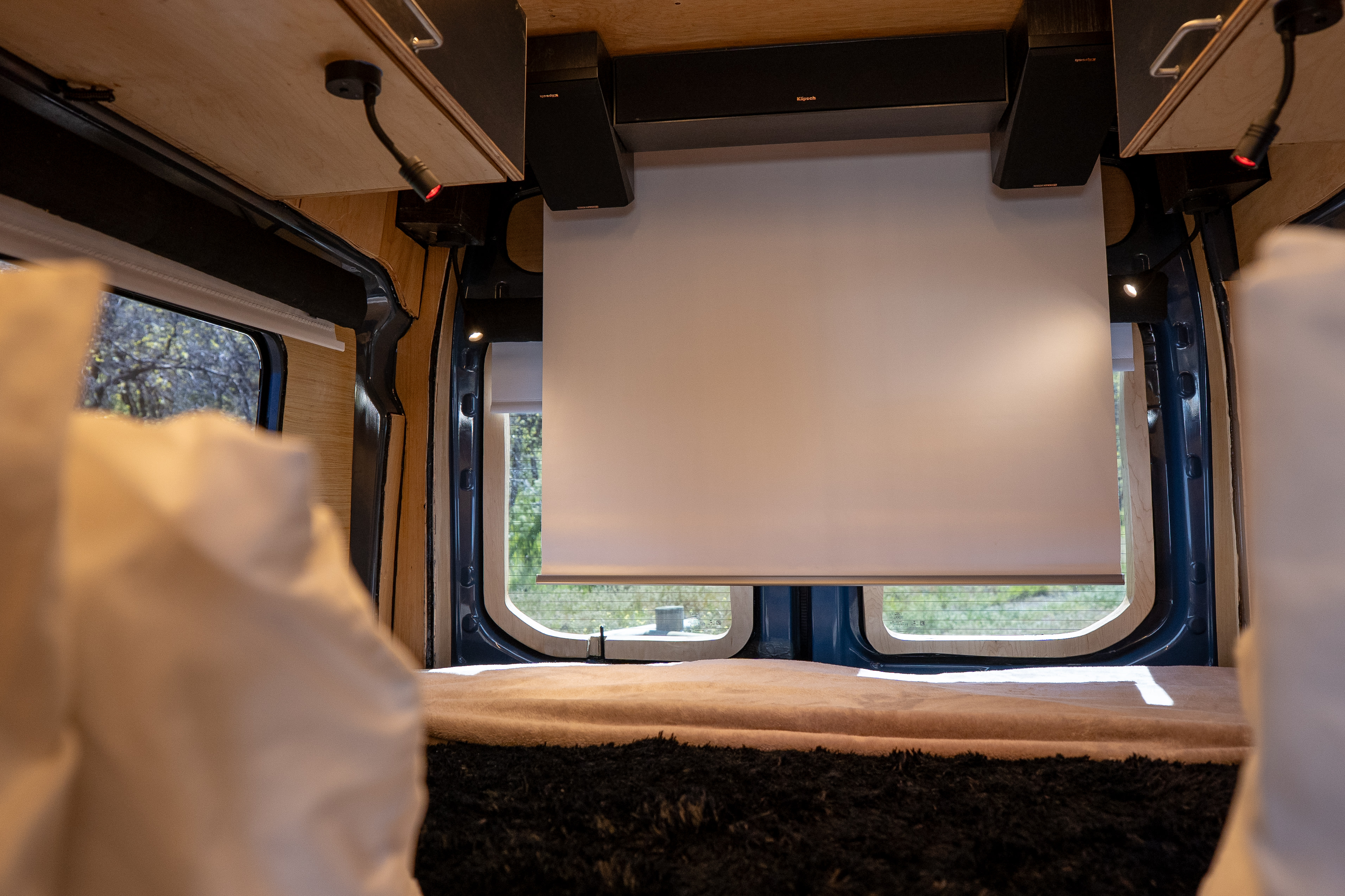 Experience an RV rental! Van interior with a pull-down screen, speakers, and comfy bed for a cozy mobile entertainment setup.. Ford Custom 2019