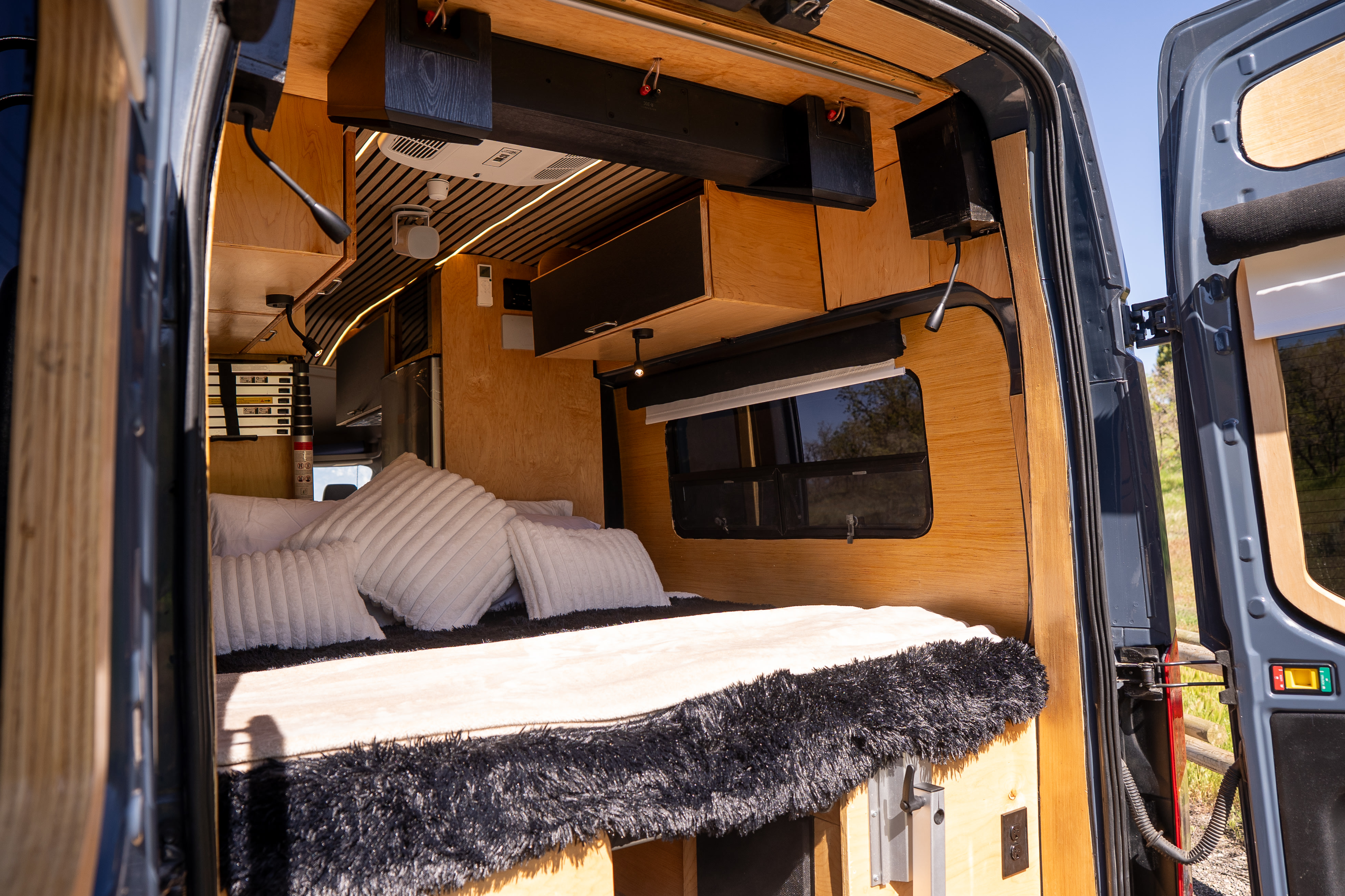 Cozy rv rental interior: A custom-built camper van with a bed, wooden walls, and modern amenities, viewed from the open back doors.. Ford Custom 2019
