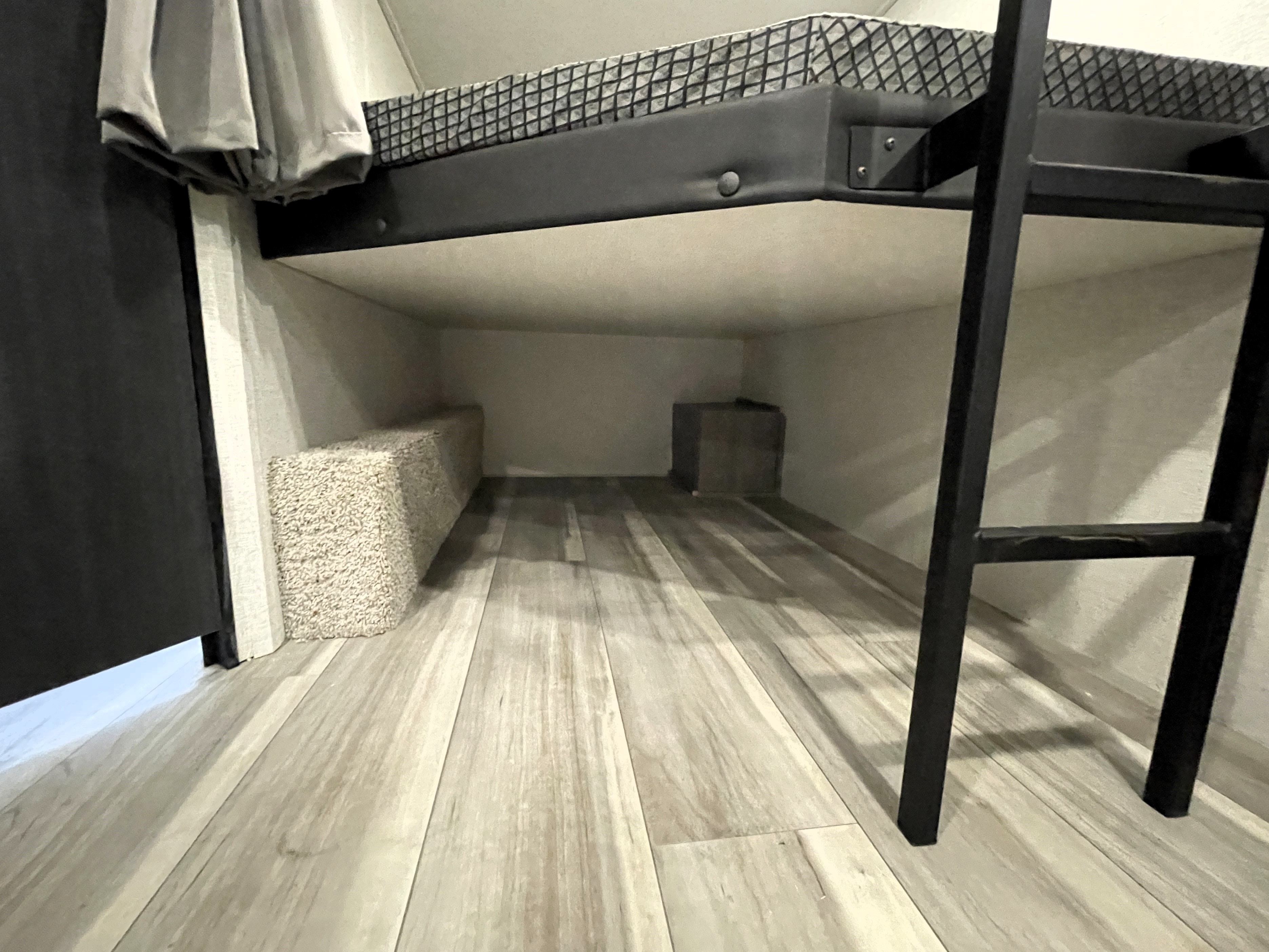 RV rental bunk bed's lower level offers ample storage: a soft textured bench and a small cube on a wood-style floor.. Keystone RV Hideout Sport 2024