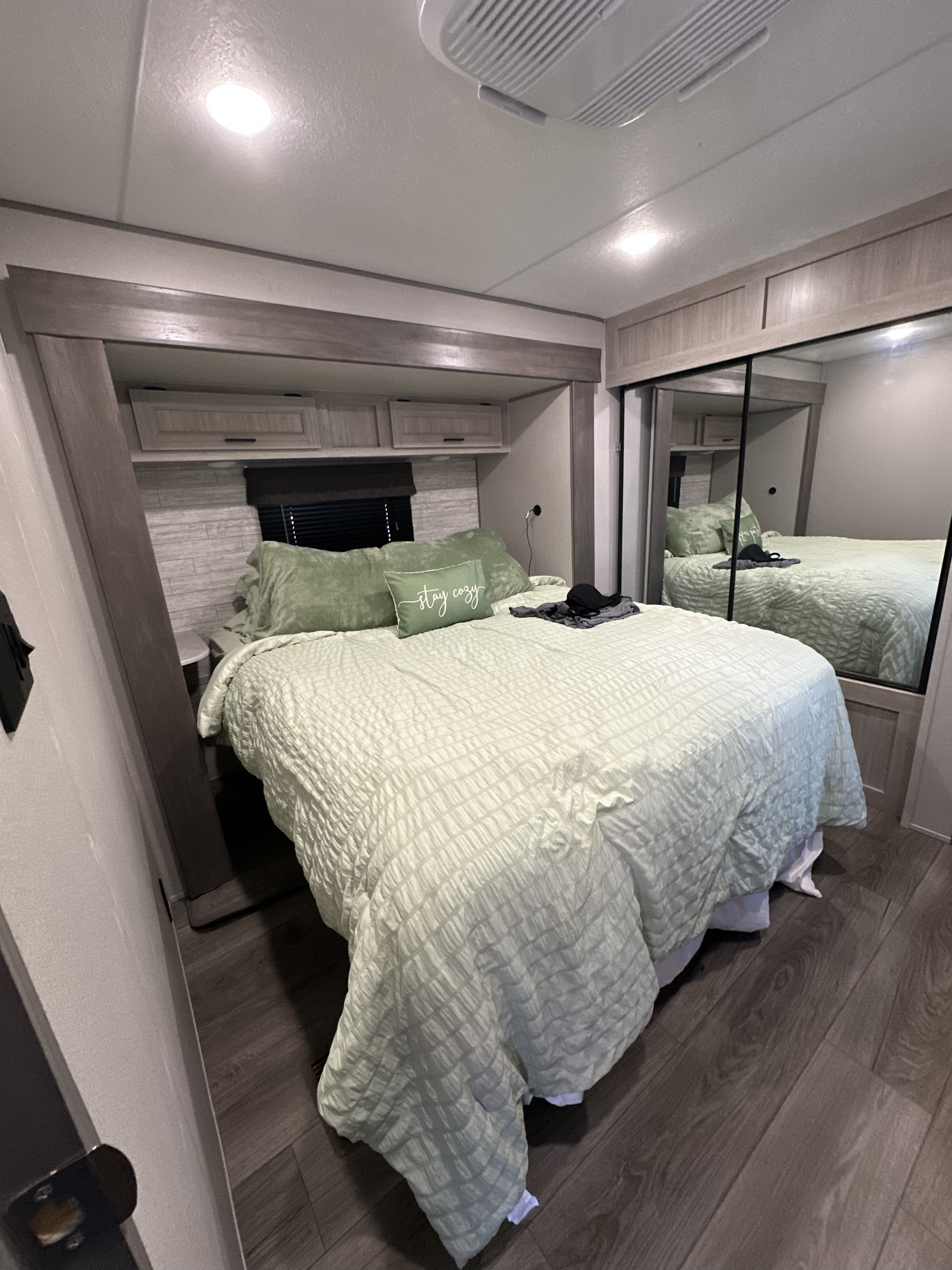 Comfortable rv rental bedroom with light green bed, overhead cabinets, mirrored closet & AC. Stay cozy on your trip.. Forest River Coachmen Catalina Legacy 2025