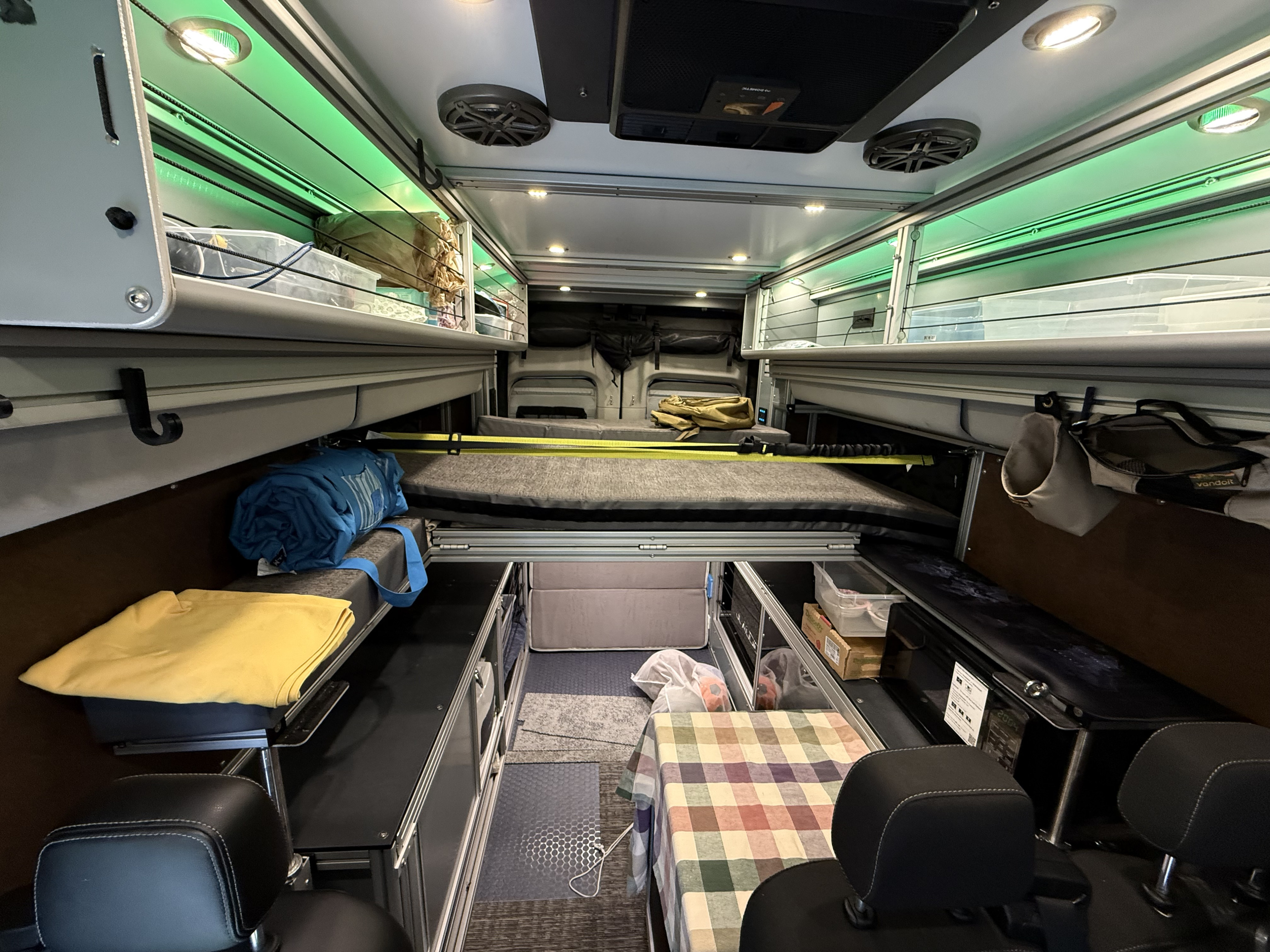 RV rental interior features a modular bed, overhead green-lit storage, and seating, offering a compact living space.. Ford Transit 2020