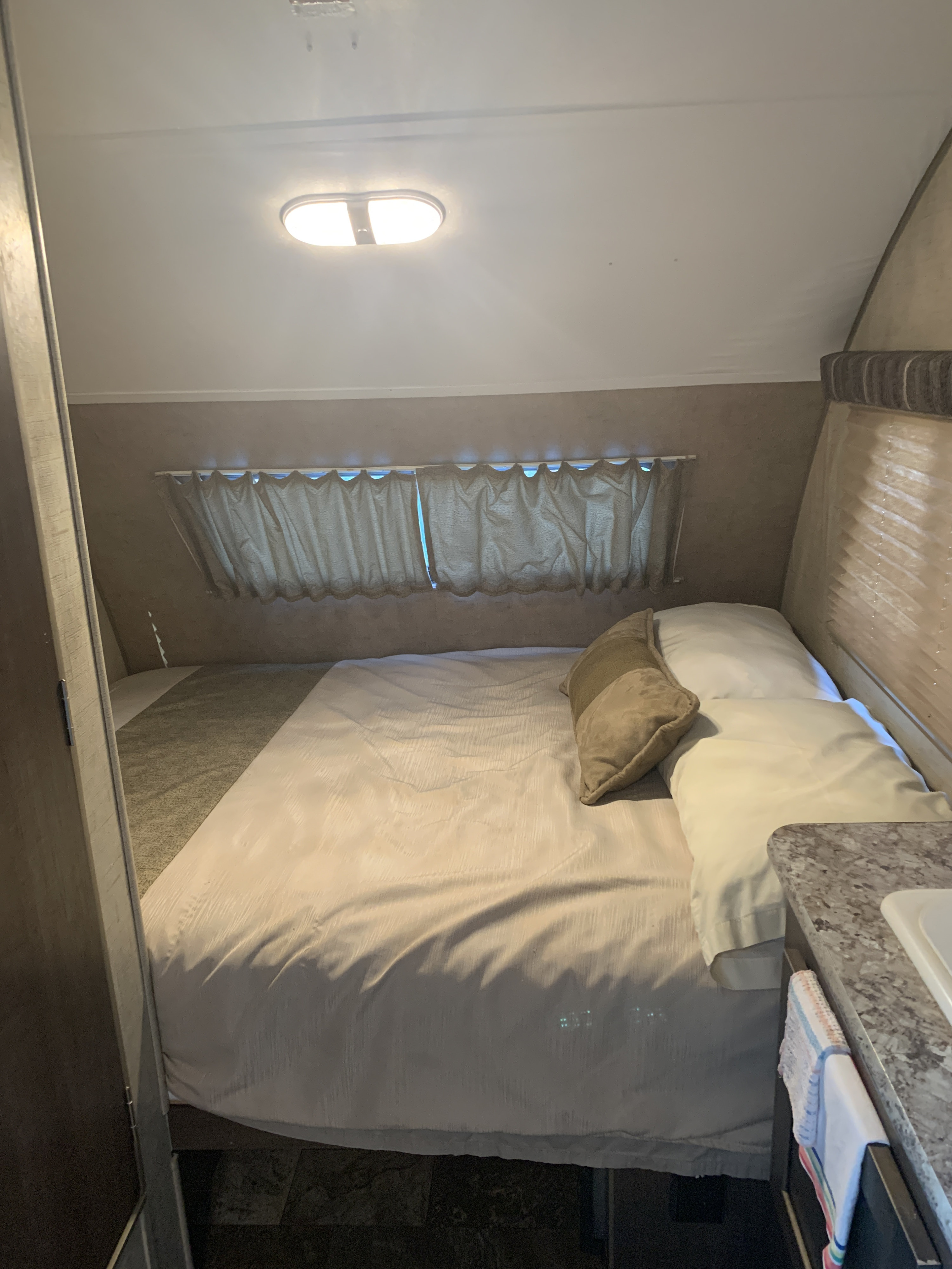 Comfortable RV rental bedroom interior with a neatly made bed, window curtains, and a partial sink counter.. Forest River Rpod 2016