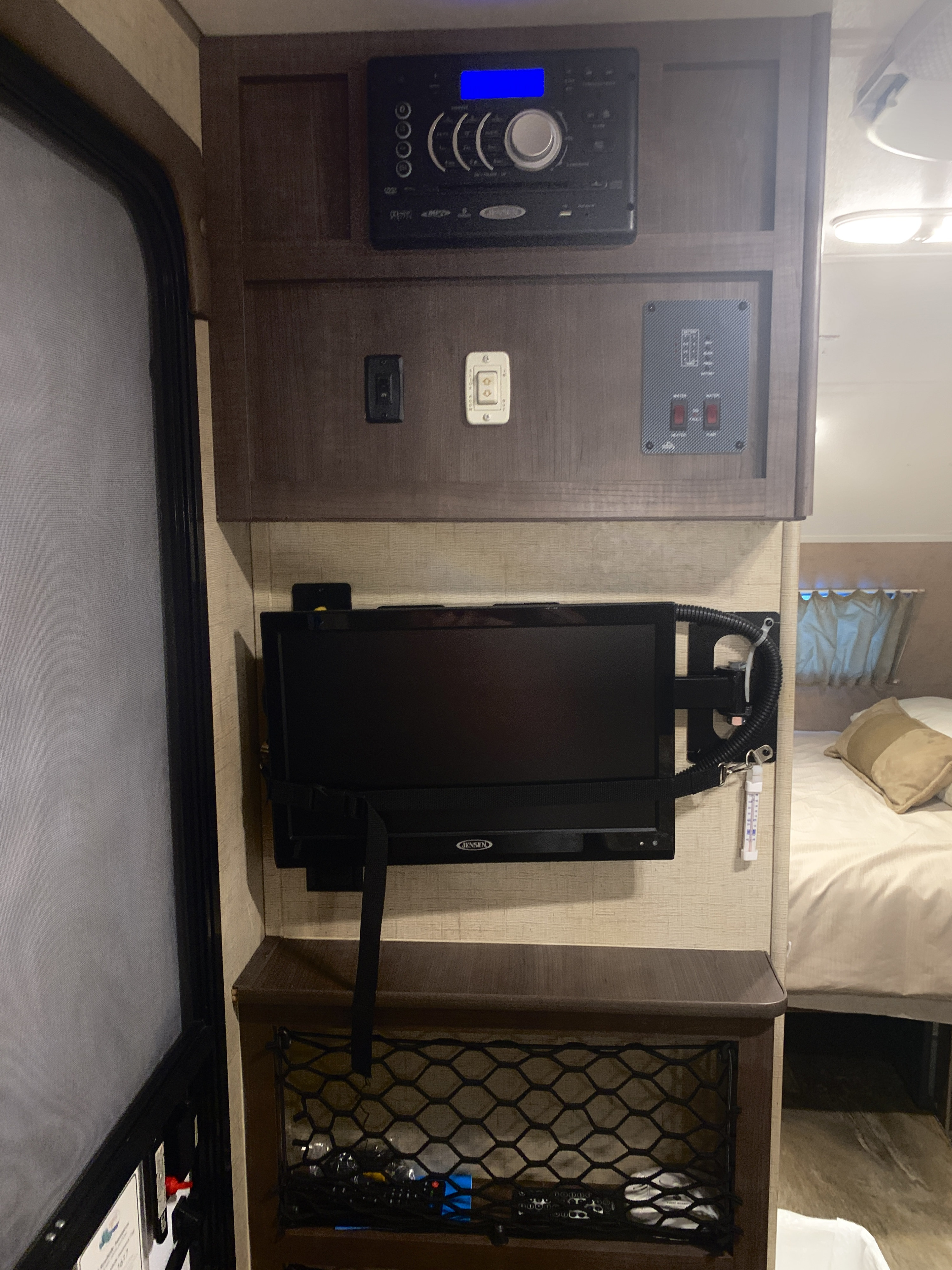 RV rental interior showing a Jensen TV, stereo system, control panel, and a cozy bedroom view.. Forest River Rpod 2016