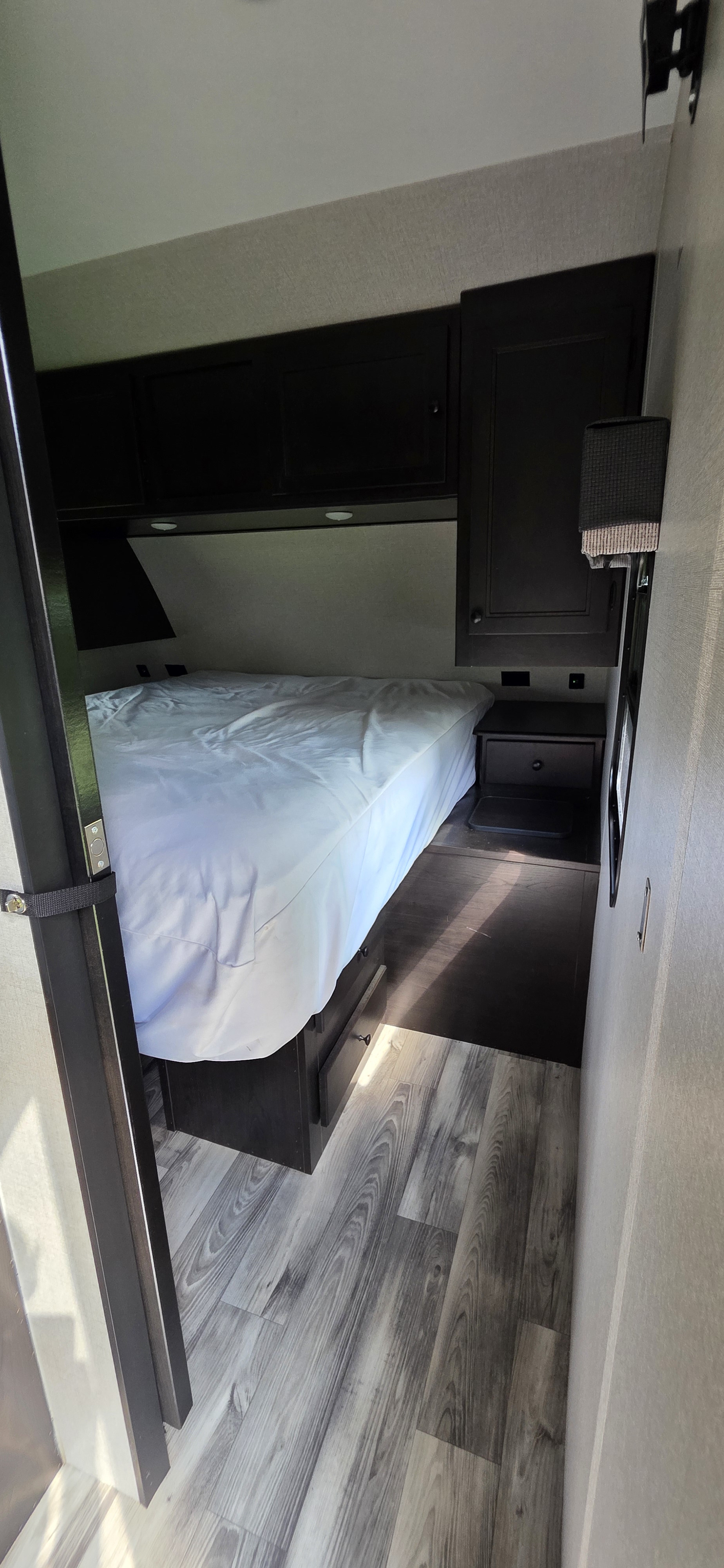 Cozy rv rental bedroom interior with dark overhead cabinets, white bedding, and wood-look flooring, viewed from the doorway.. Starcraft Super Lite 2022