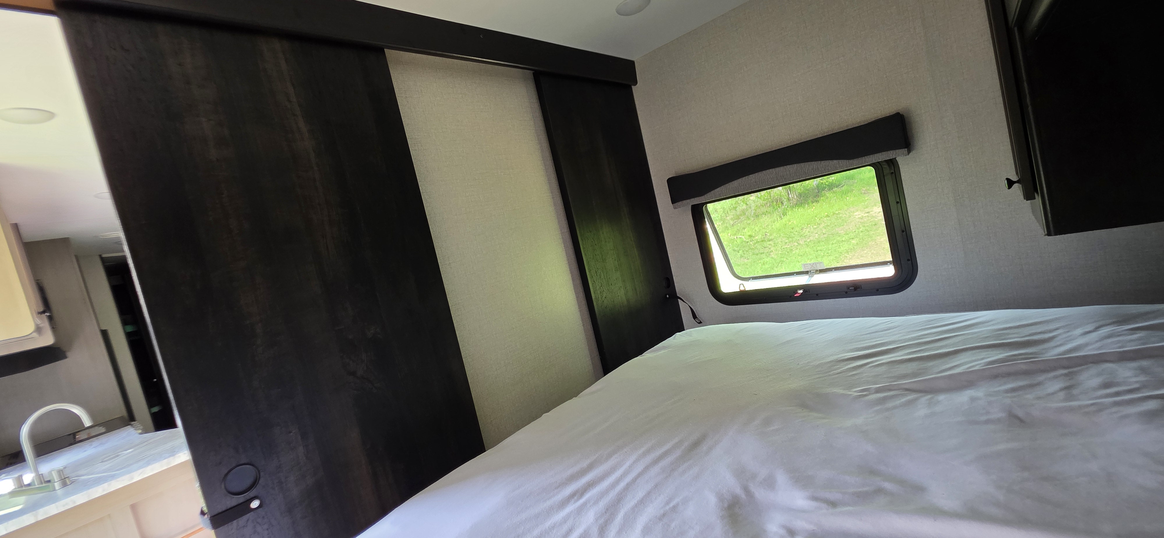 RV rental bedroom featuring a comfortable bed, open window with green views, and sliding doors to the kitchen.. Starcraft Super Lite 2022