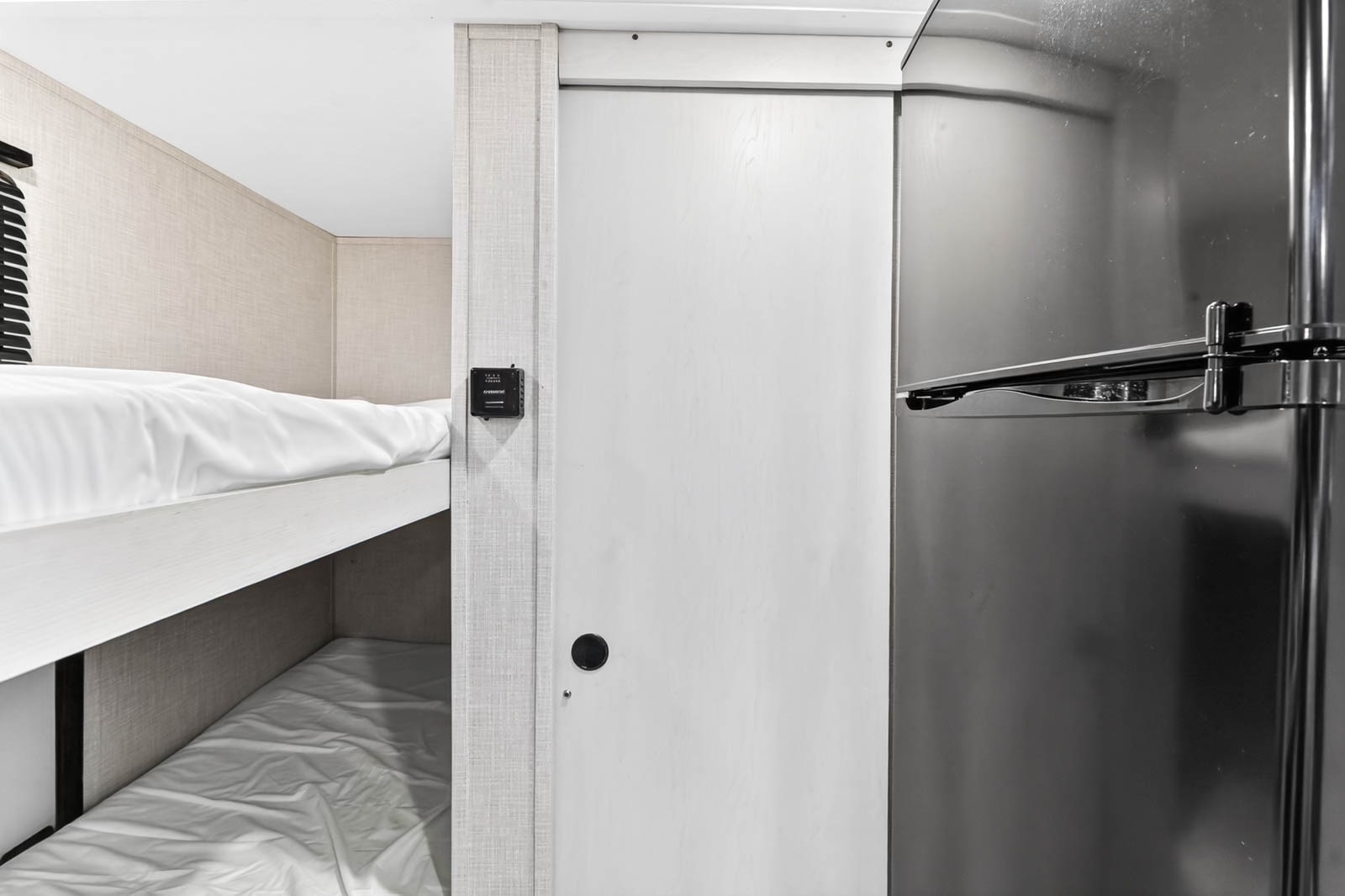 Compact RV rental interior featuring cozy bunk beds, a space-saving sliding door, and a stainless steel refrigerator.. Dutchmen Coleman Rubicon 2022