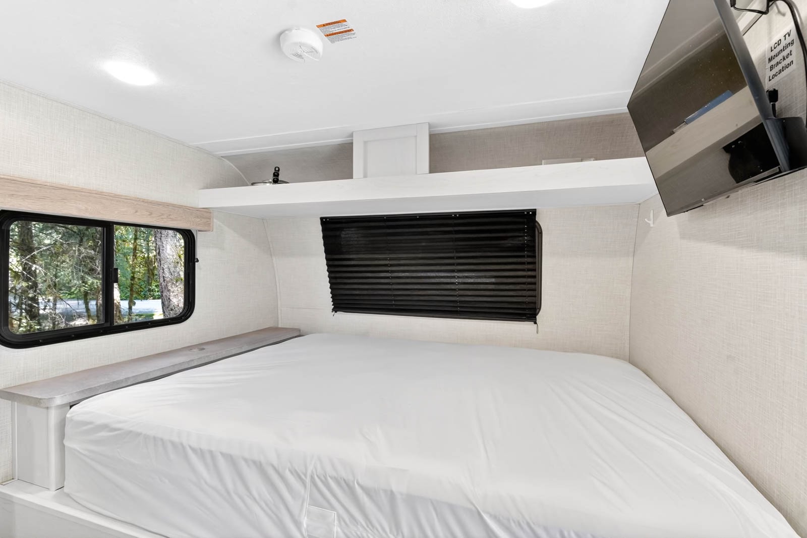 Cozy rv rental bedroom features a comfortable bed, window views, overhead storage, and a wall-mounted TV.. Dutchmen Coleman Rubicon 2022