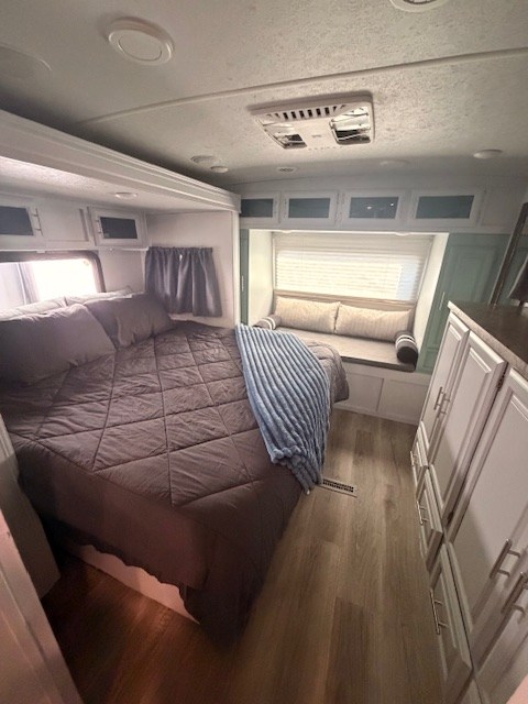 Bright RV rental bedroom features a cozy bed with dark bedding, a window seat, modern cabinets, and light wood-look flooring.. Forest River Flagstaff Super Lite 2021