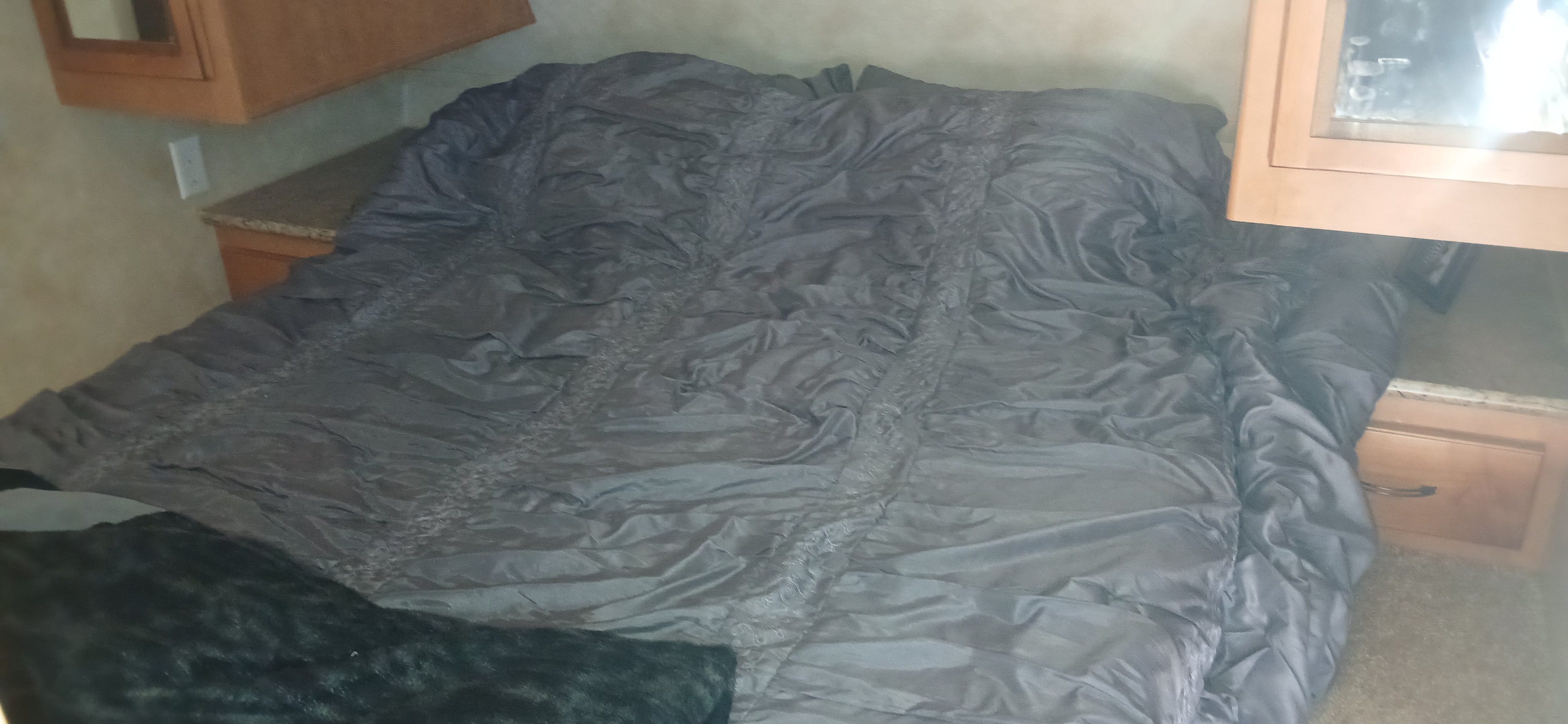 Inside an RV rental, a bed with a dark grey comforter and fuzzy blanket. Built-in wooden cabinets provide storage in this cozy bedroom.. Palomino Puma 2013