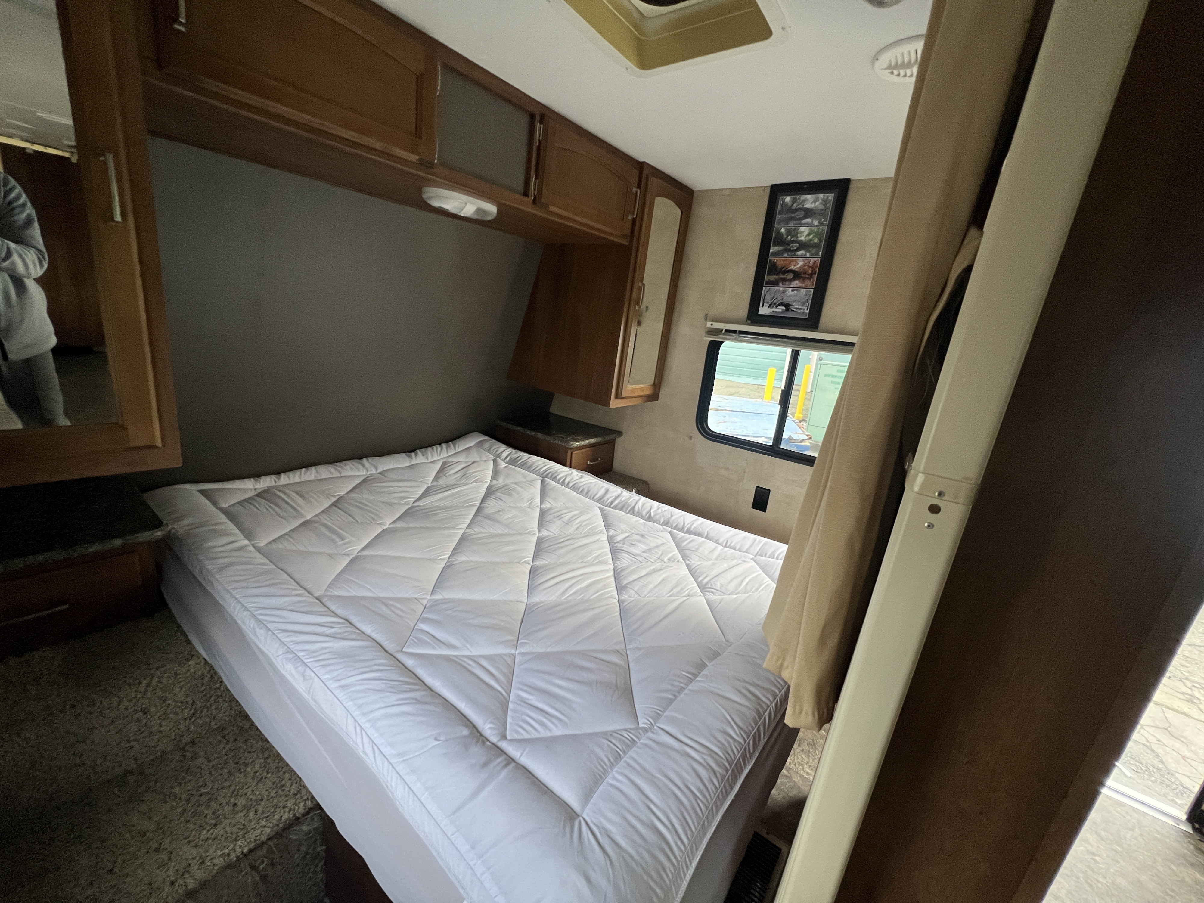 Cozy RV rental bedroom with a comfortable bed, overhead storage, and window, perfect for your next adventure.. Keystone RV Springdale 2015