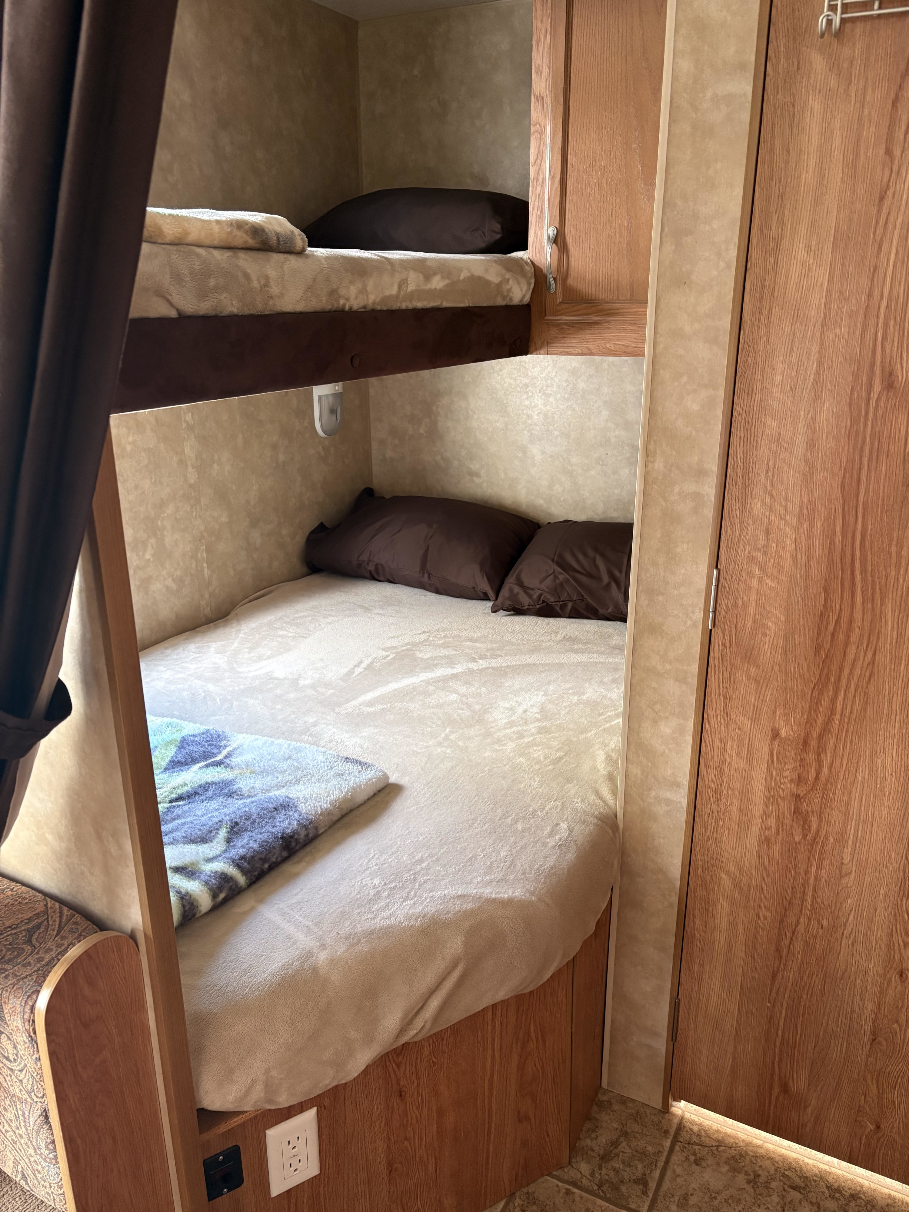 RV rental interior shows bunk beds with soft bedding, dark pillows, wooden panels, and an electrical outlet, offering compact sleeping space.. Jayco Jay Flight 2010