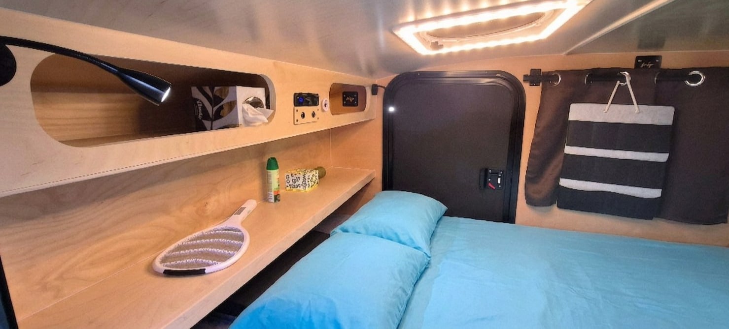 Experience this cozy RV rental's compact interior, featuring a comfy bed, functional storage, and warm lighting.. Hiker Trailer Backcountry Trailer (Mid Range XL) 2022