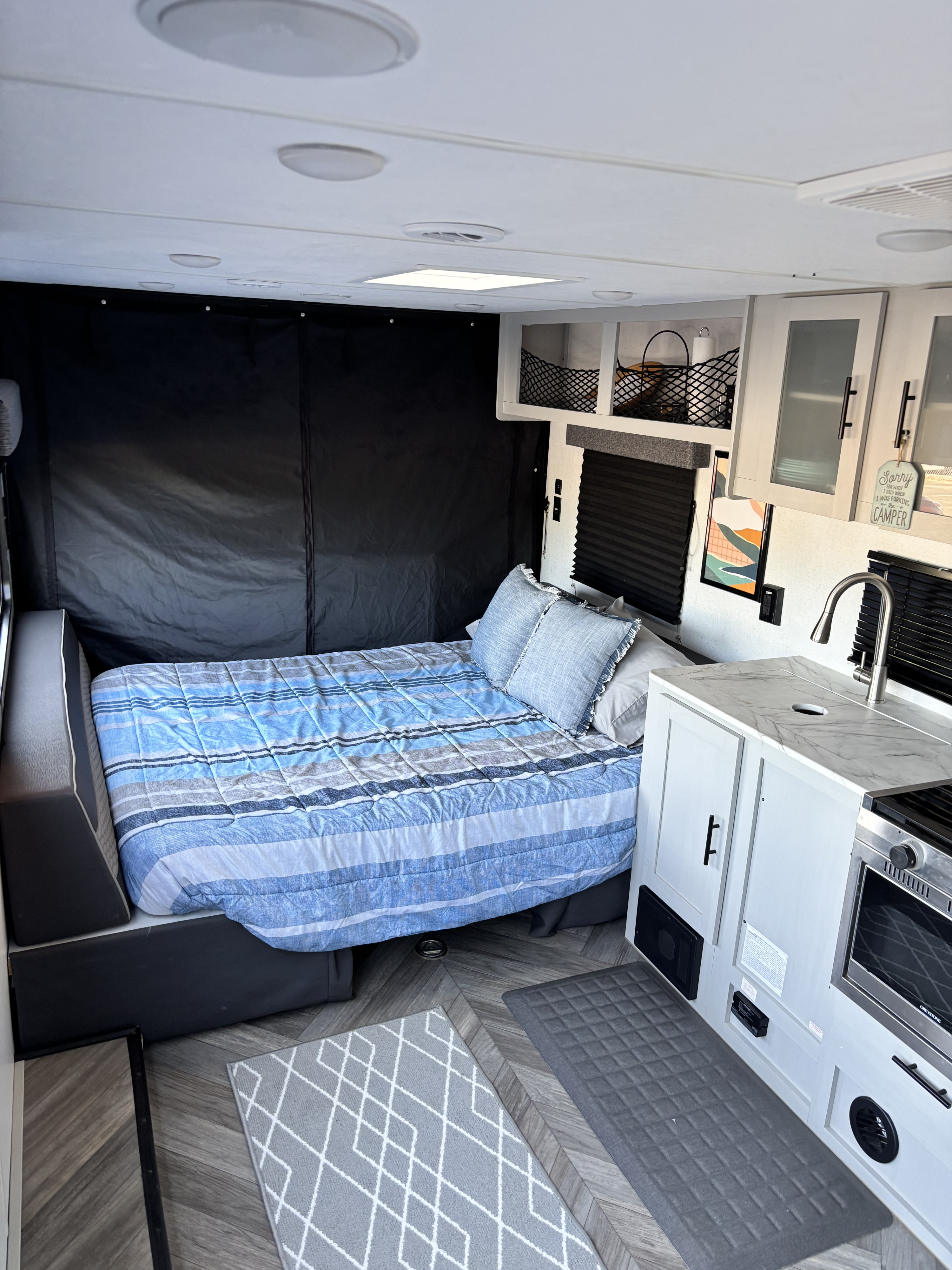 Cozy rv rental interior with a bed featuring blue striped bedding, a compact kitchen with a sink, and herringbone flooring.. Forest River Salem FSX Platinum Toy Hauler 2022