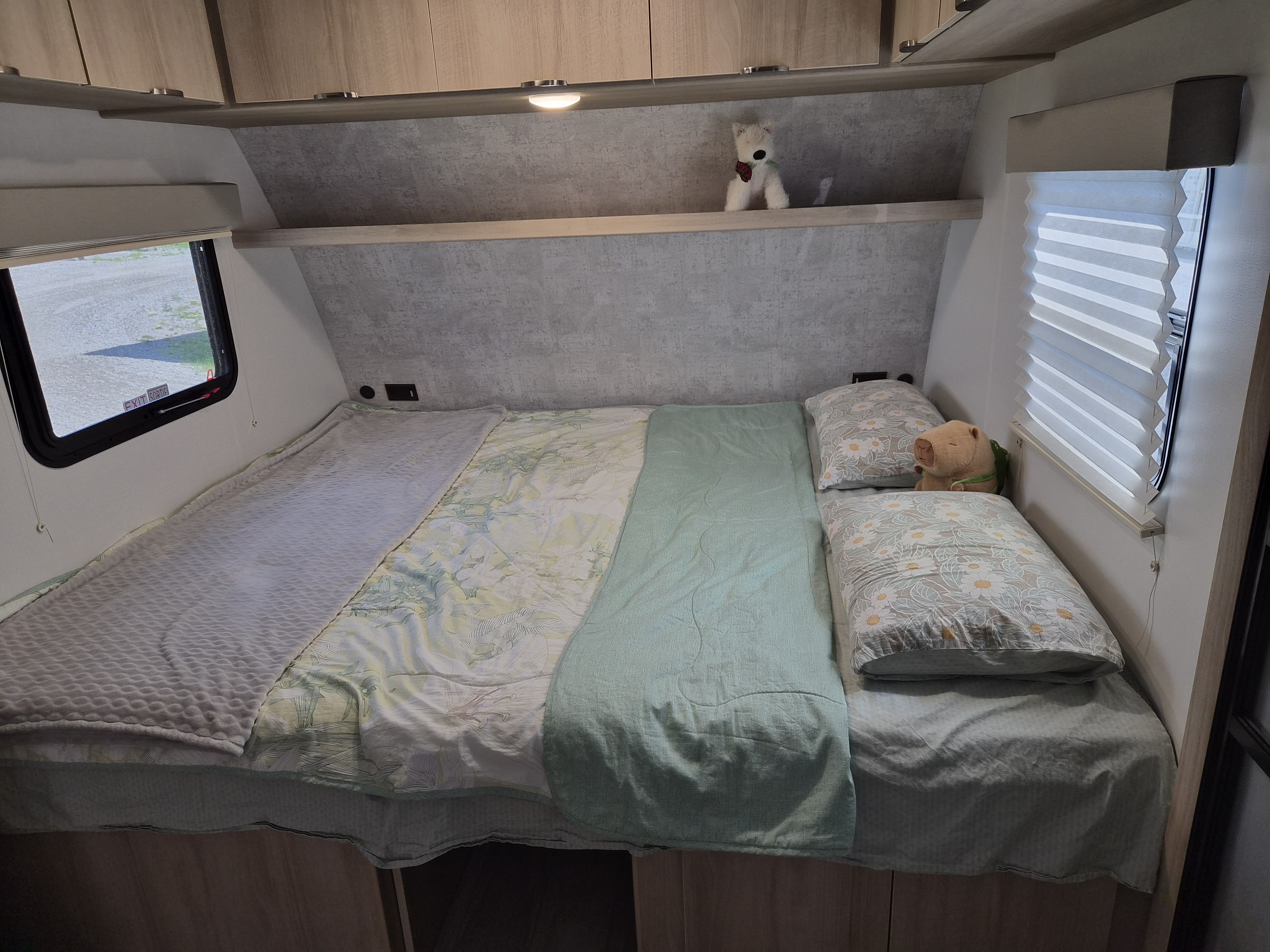 An rv rental bedroom: a bed with mint green and floral bedding, pillows, and overhead storage for a cozy stay.. Winnebago Micro Minnie 2108TB 2022