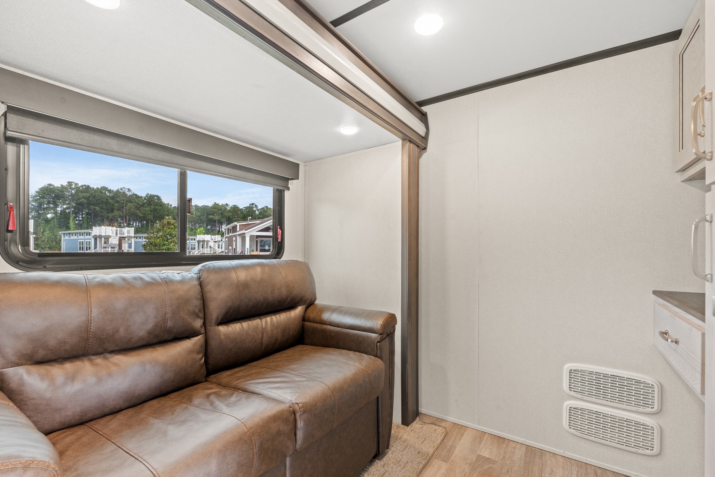 RV rental interior: comfy brown sofa, large window with outdoor views of a park, plus cabinetry and floor vents.. Keystone RV Montana High Country 2021