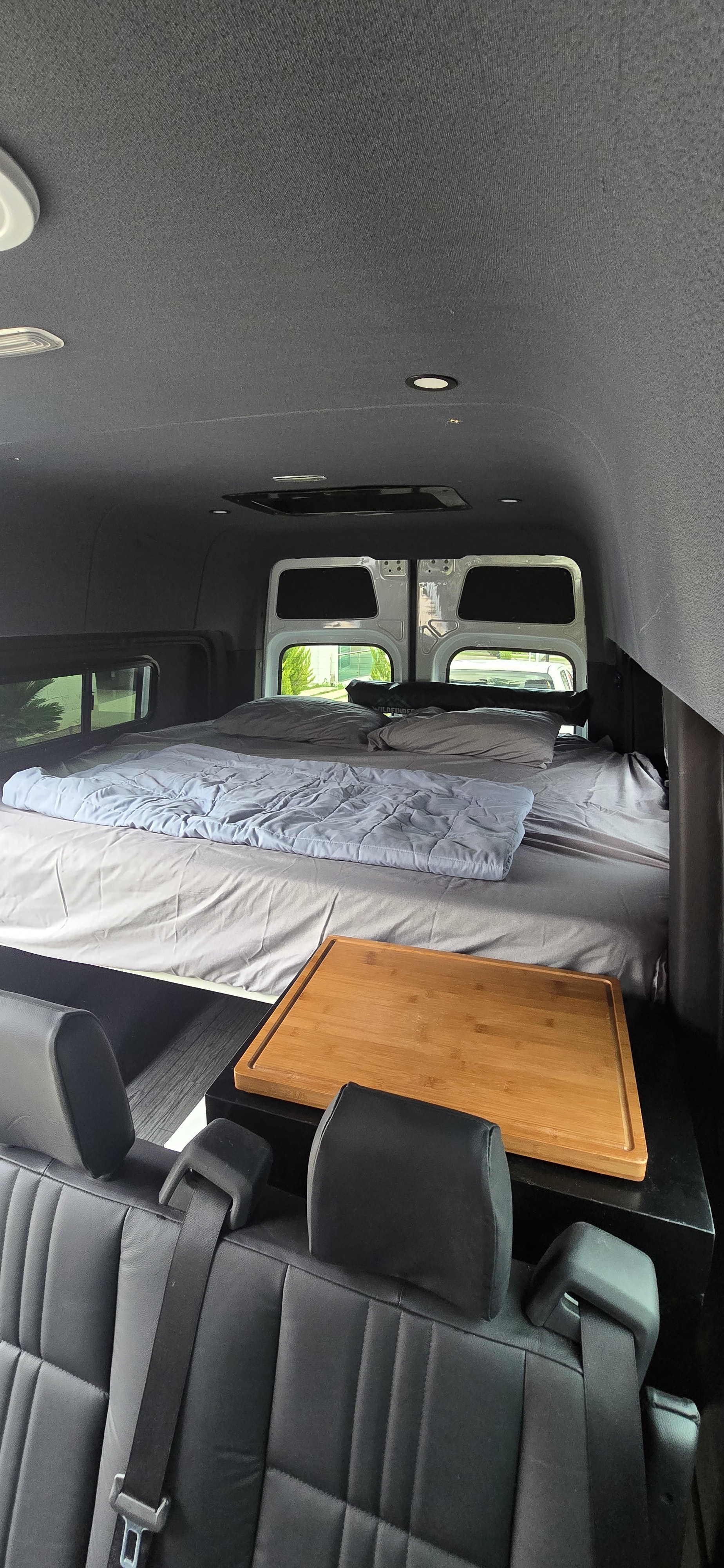 Cozy rv rental interior: elevated sleeping area, bedding, and wooden tray. Ideal for camper van adventures.. Mercedes Sprinter 2023