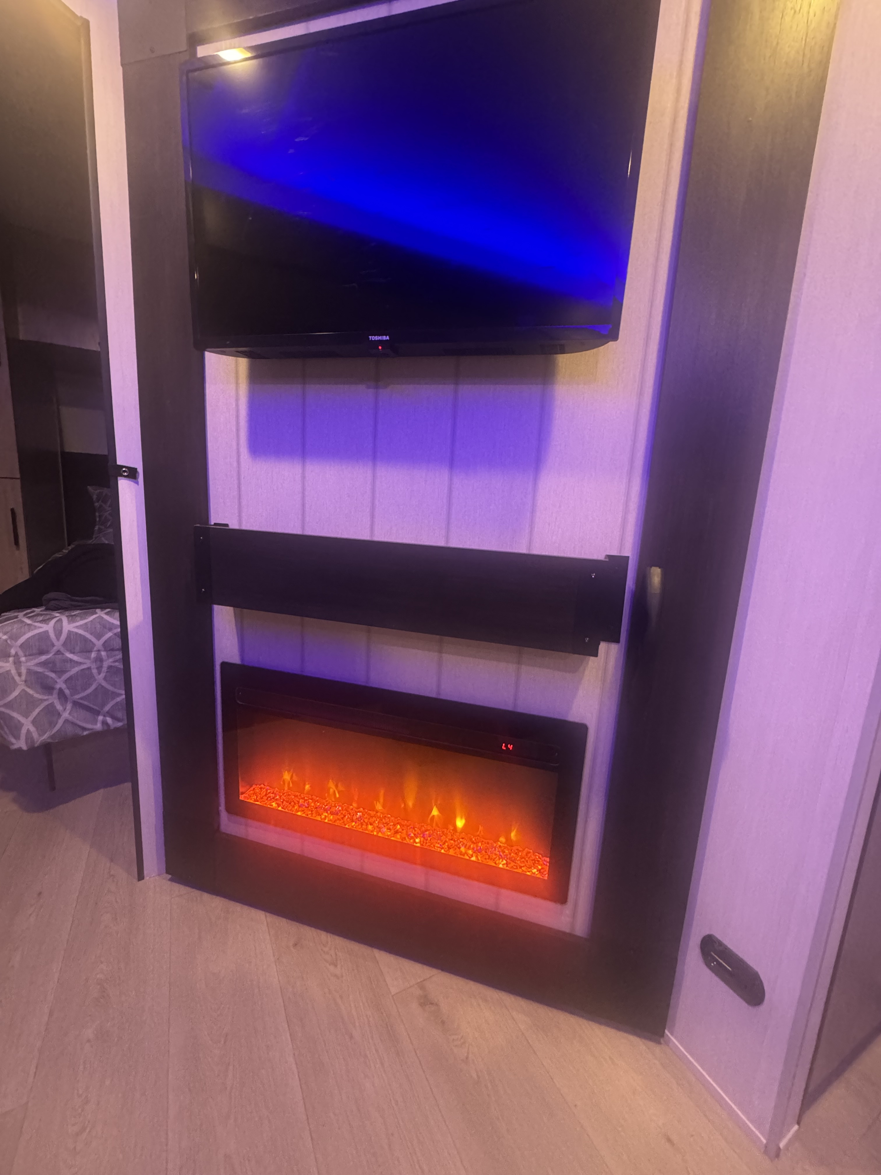 Cozy RV rental interior with a TV, soundbar, and an inviting electric fireplace. Adjacent bedroom space is visible.. Forest River 26KF 2026