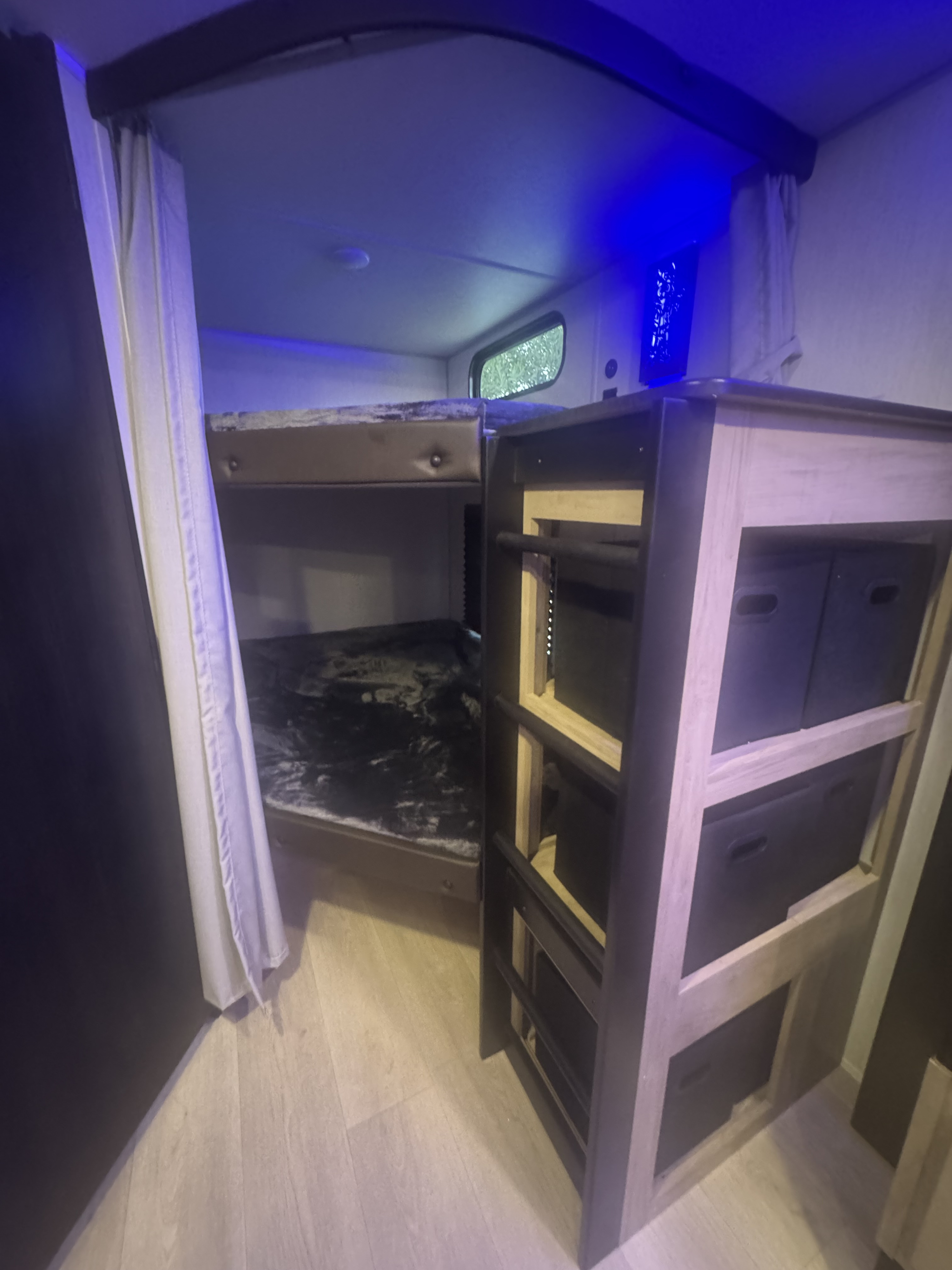 Inside an RV rental: double bunk beds with plush bedding, a storage cabinet with bins, and soft blue lighting.. Forest River 26KF 2026